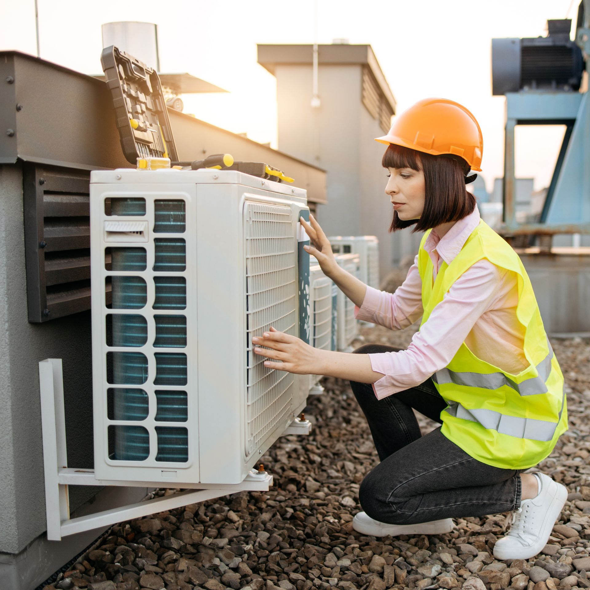 A woman is working on an air conditioner on the roof of a building.