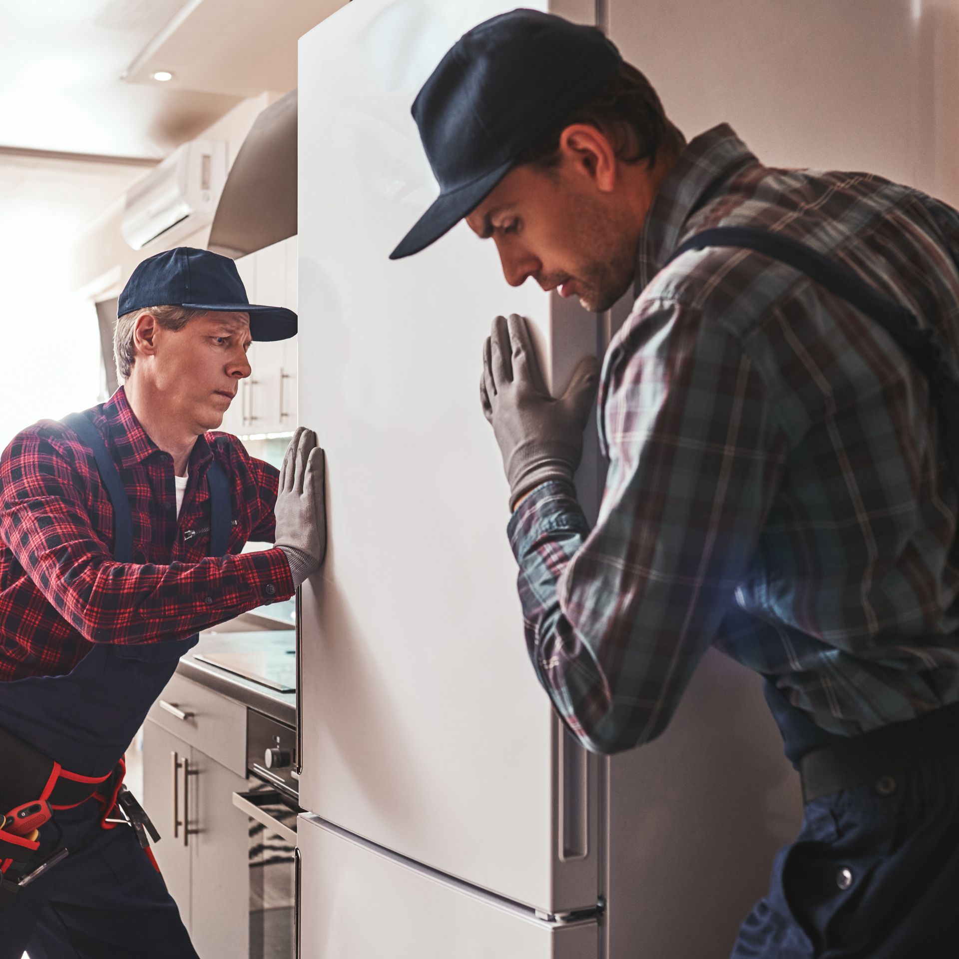 Two men are working on a refrigerator in a kitchen.