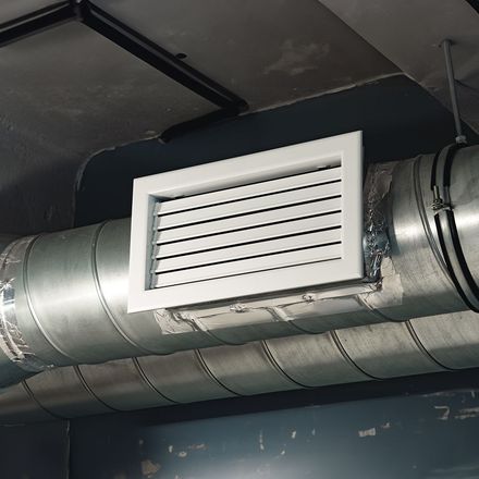 A white air vent is hanging from the ceiling of a metal pipe.