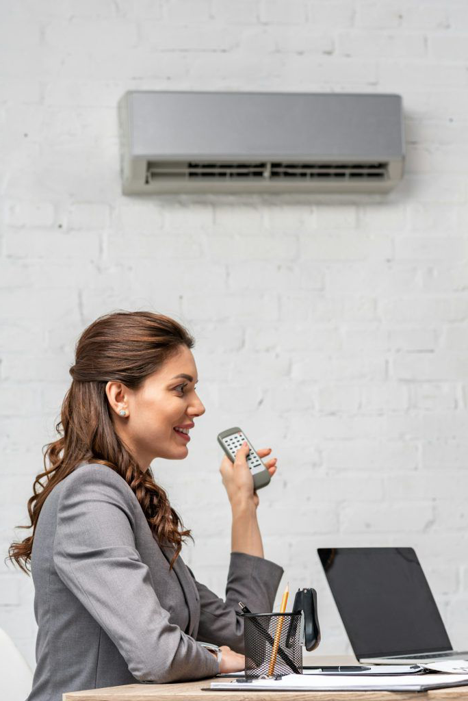 A woman is sitting at a desk holding a remote control.