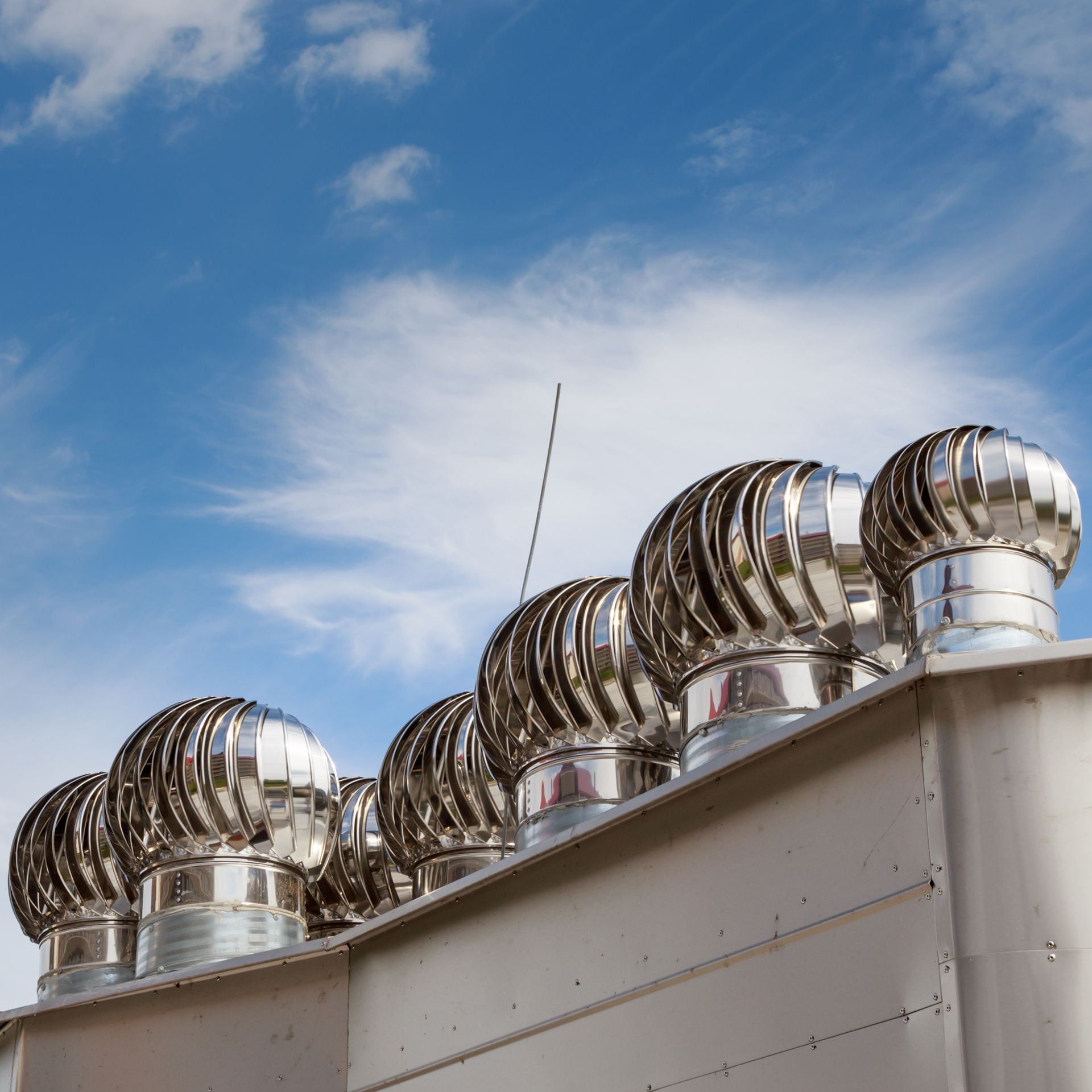 A row of stainless steel exhaust fans on top of a building.