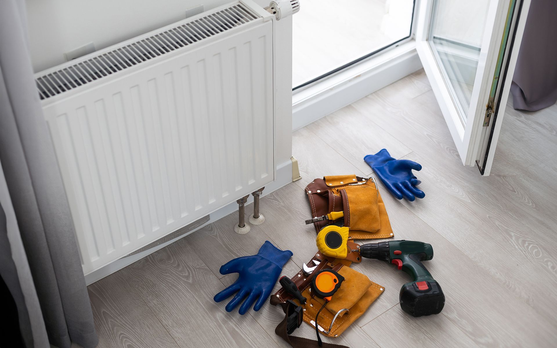 A bunch of tools are laying on the floor next to a radiator.