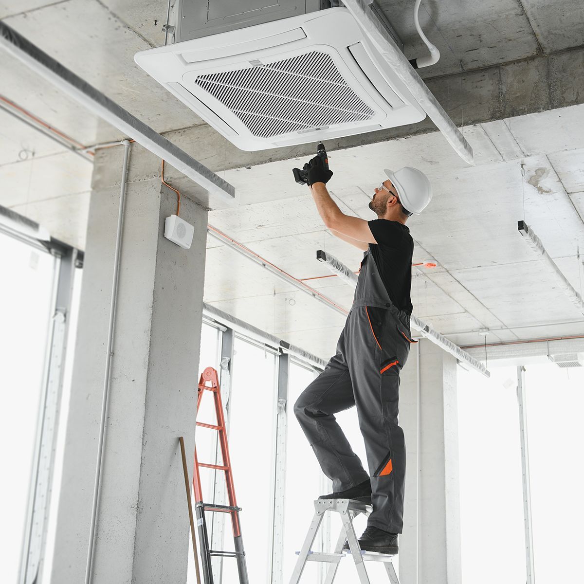 A man is standing on a ladder working on a ceiling fan.