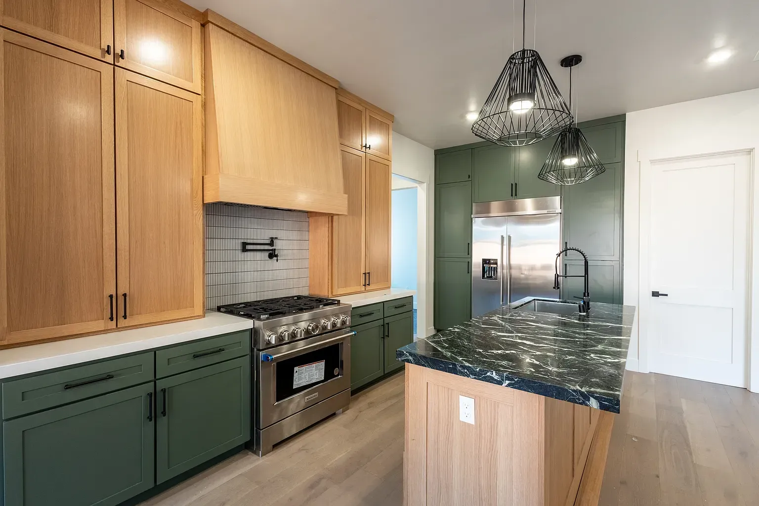 Modern kitchen with green cabinets, stainless steel appliances, and wood accents.