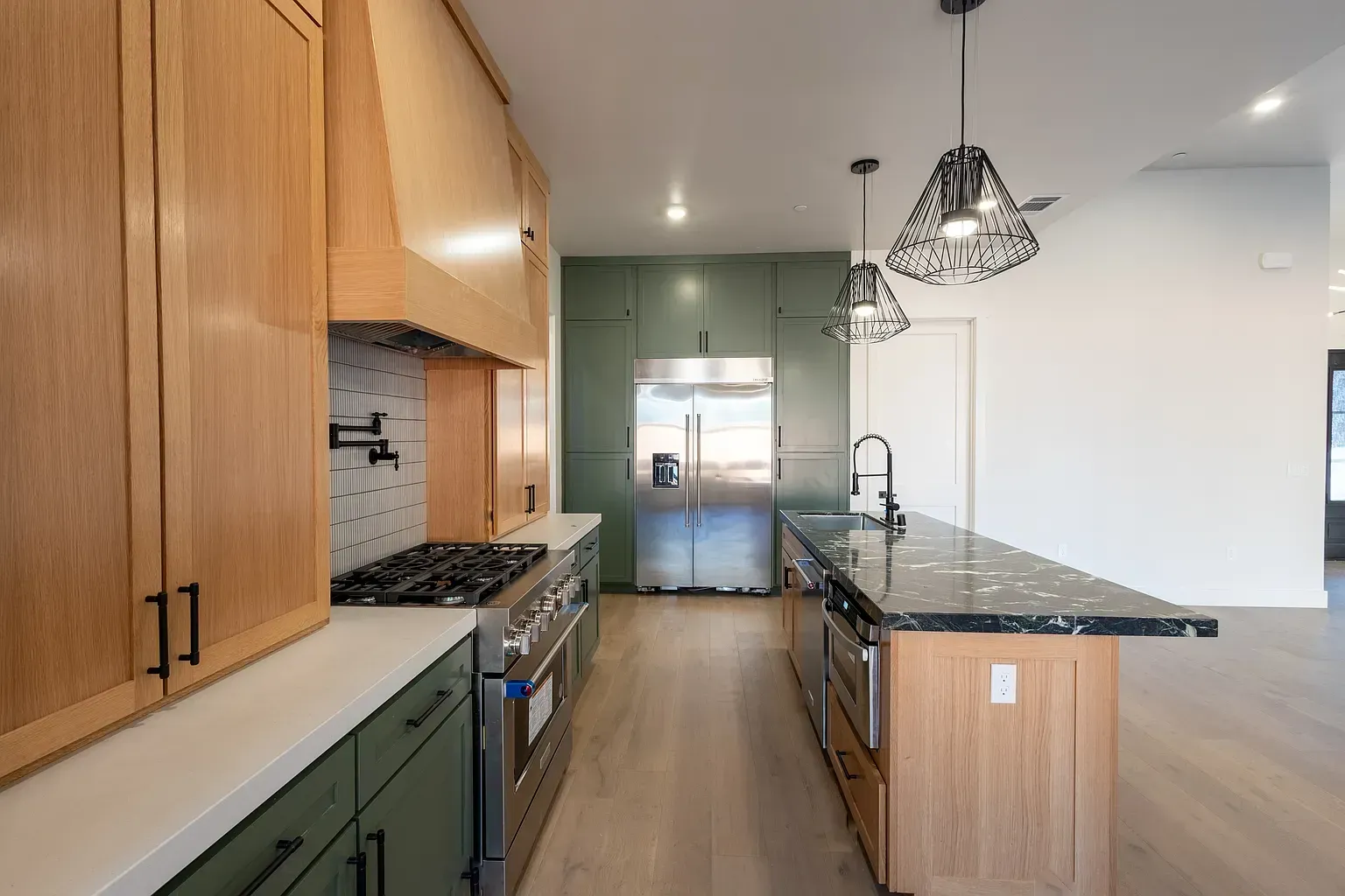 Modern kitchen with green cabinets, island, stainless steel appliances, and wood flooring.