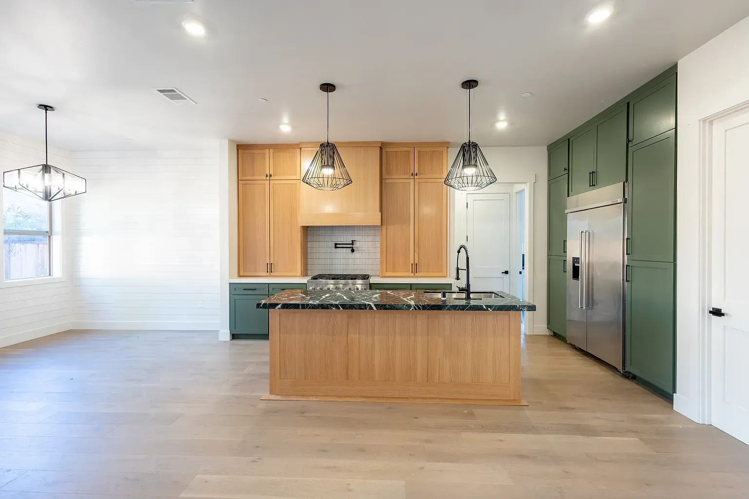 Modern kitchen with green and natural wood cabinets, granite countertops, and stainless steel refrigerator.