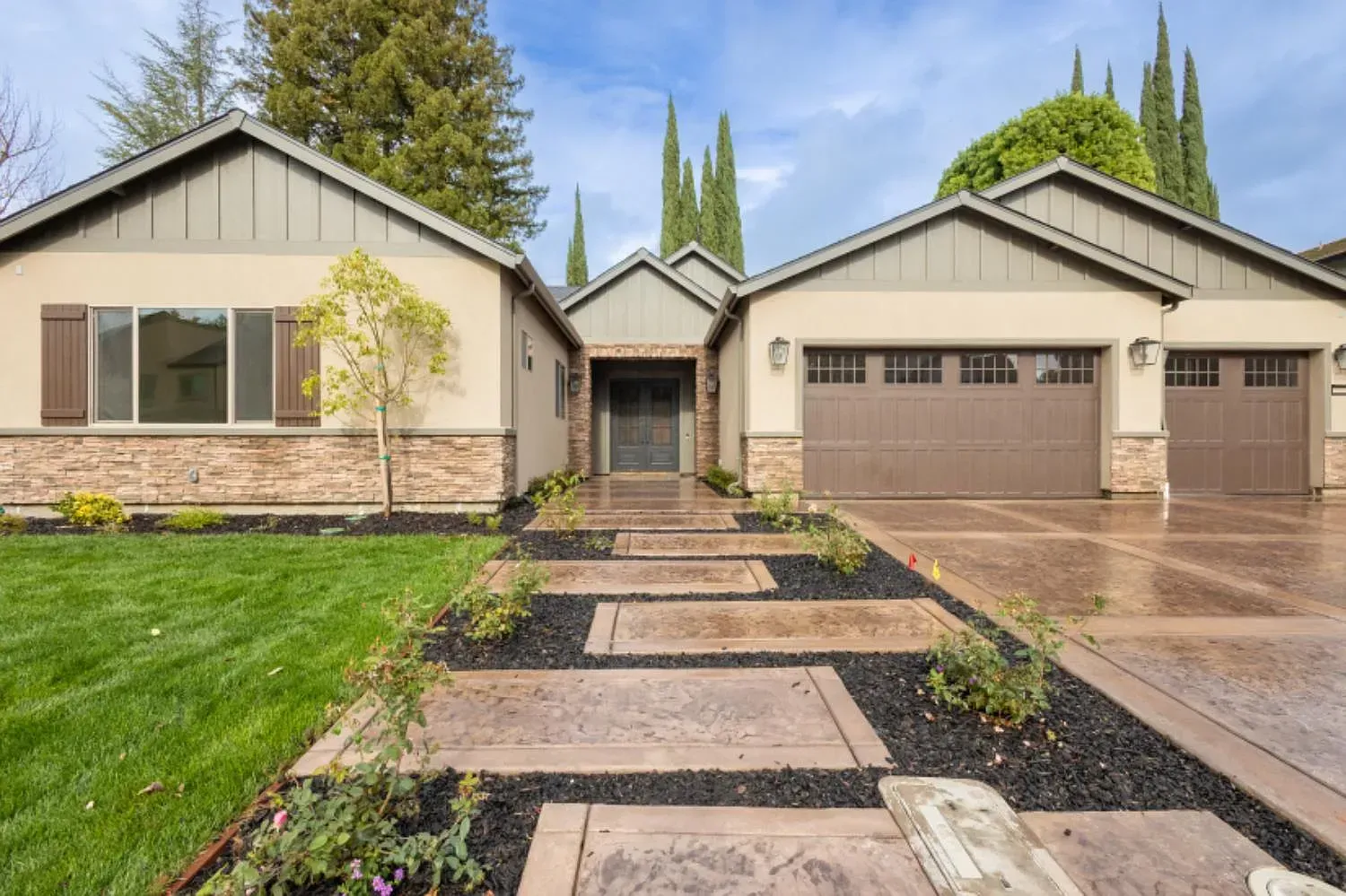 Beige and brown house exterior with stone accents, a lawn, and patterned walkway.