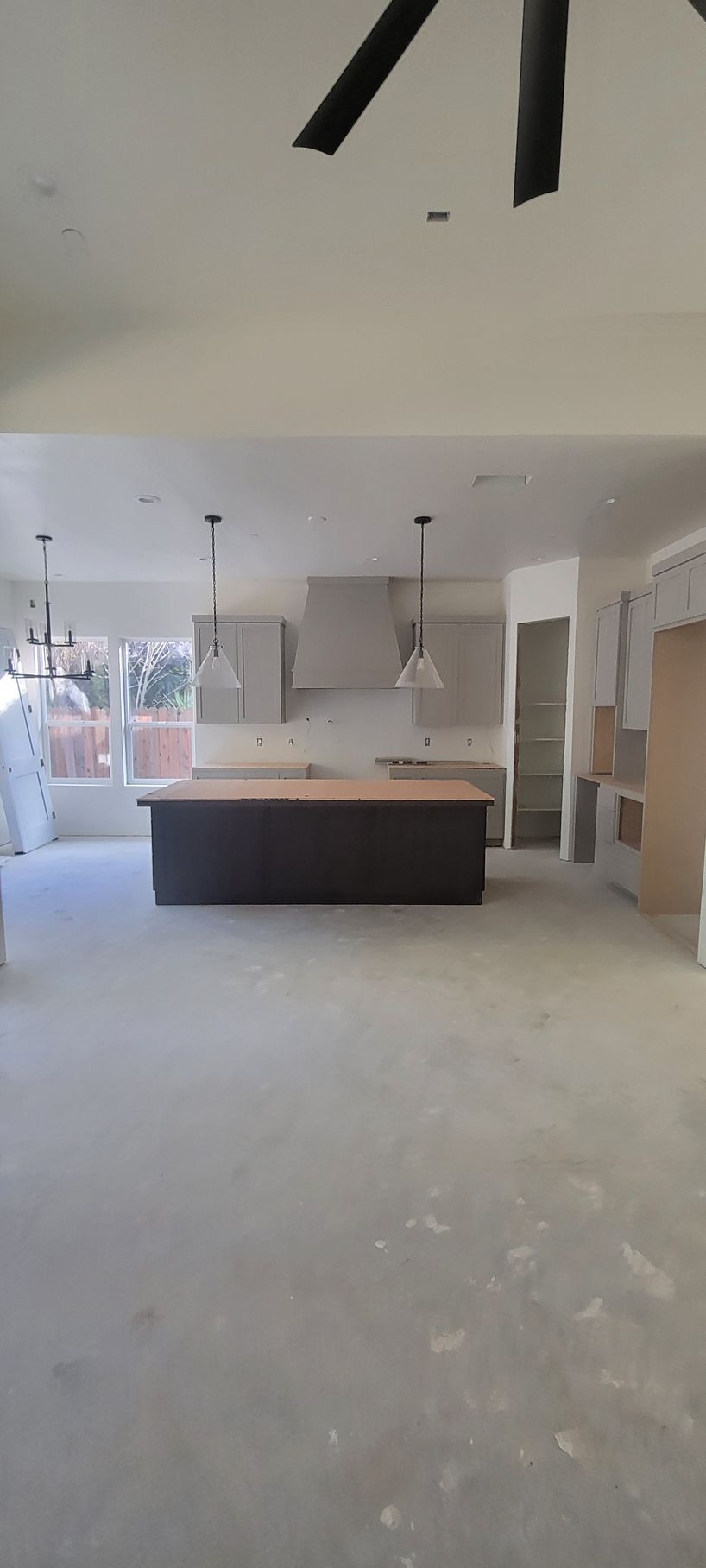 A large empty room with a kitchen and a ceiling fan.