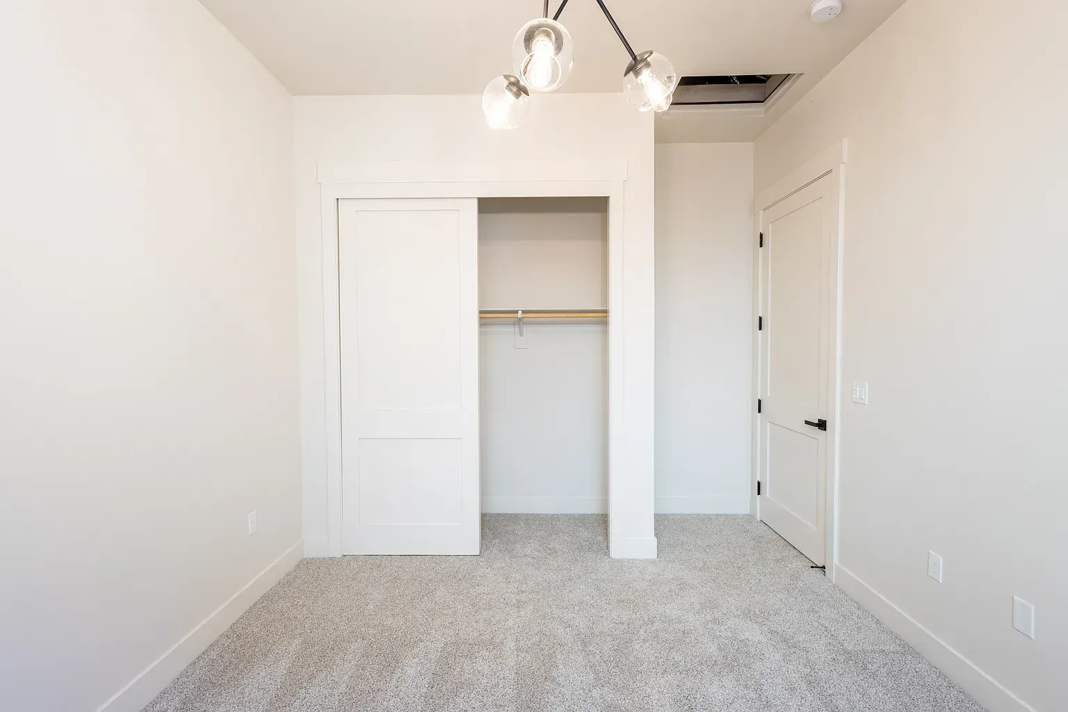 Empty room with white walls, carpet, closet, and a light fixture.