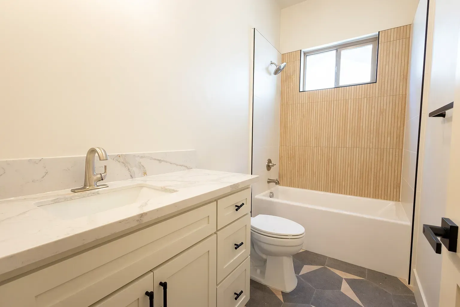 Bathroom with white vanity, tub, and toilet; wood accent wall, small window, patterned floor.