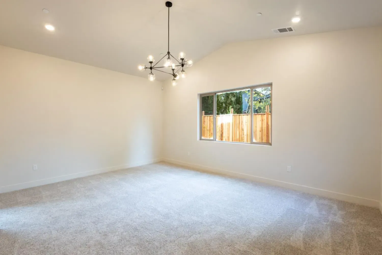 Empty room with light gray carpet, white walls, a window, and a modern chandelier.