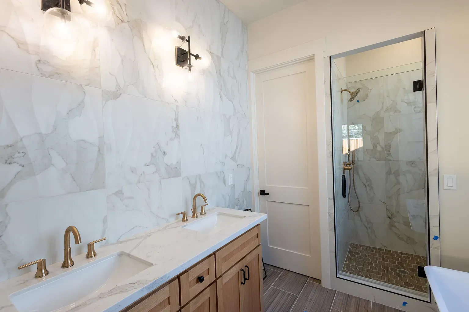 Bathroom with marble tile walls, a wooden vanity with gold fixtures, and a glass shower.