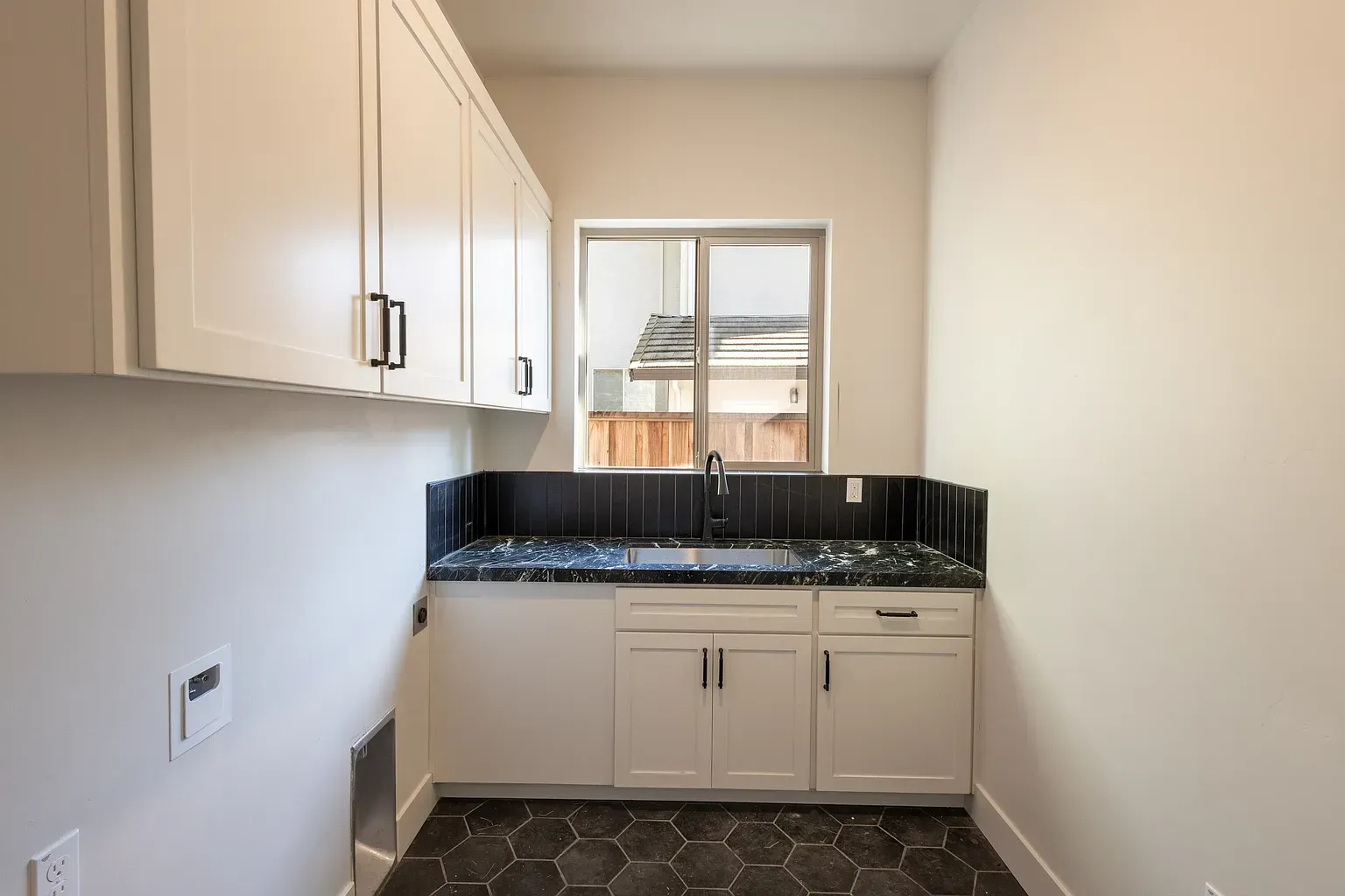 Laundry room with white cabinets, dark countertop, and window.