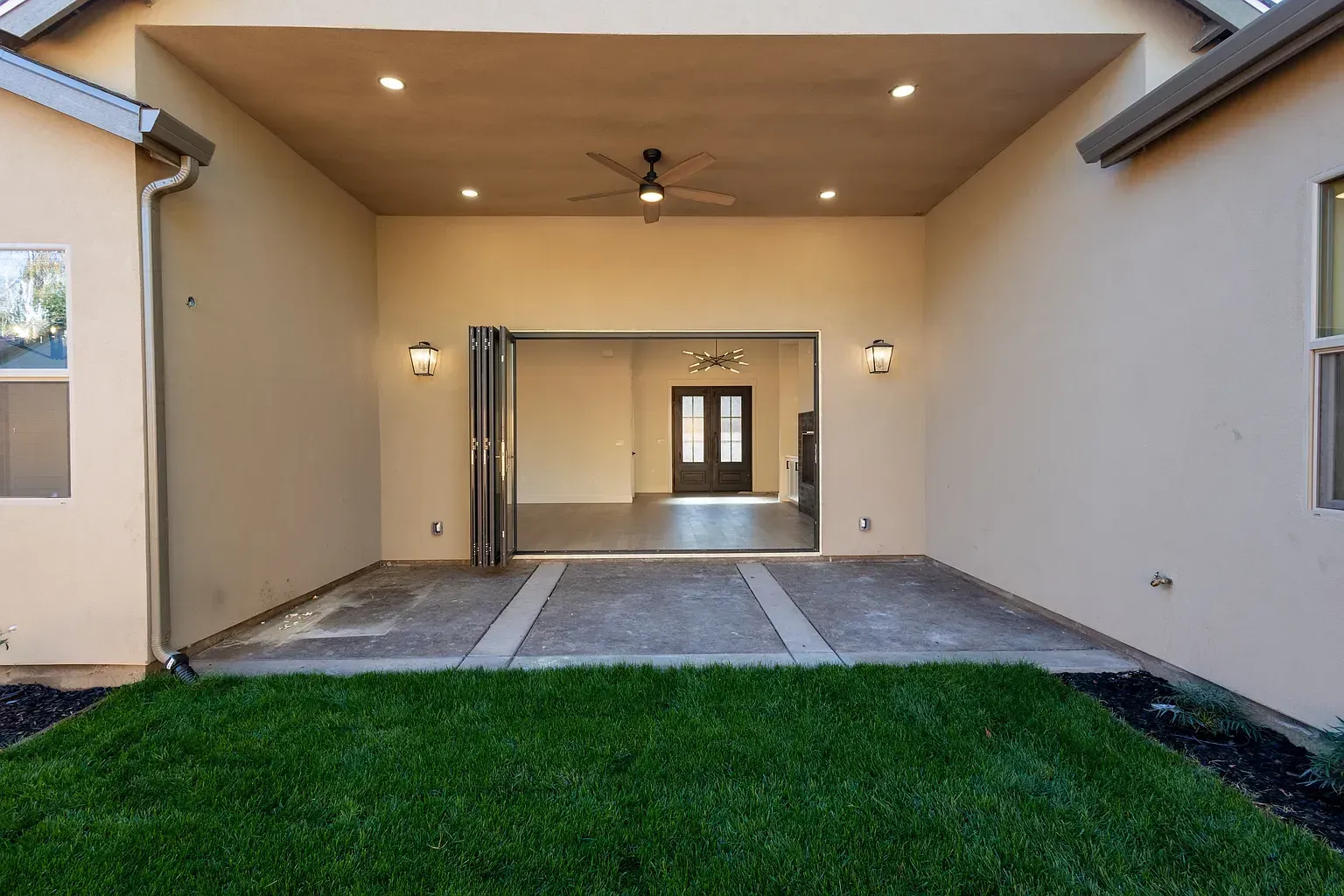 Patio with a view of an open living room. Green grass in the foreground, folding doors, and neutral wall colors.