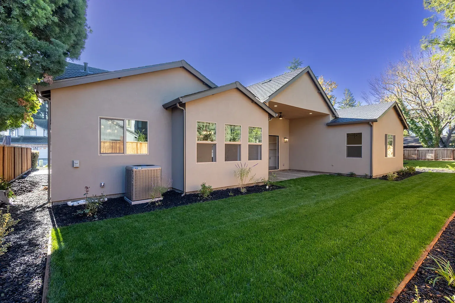 Beige house exterior with green lawn, trees, and blue sky.