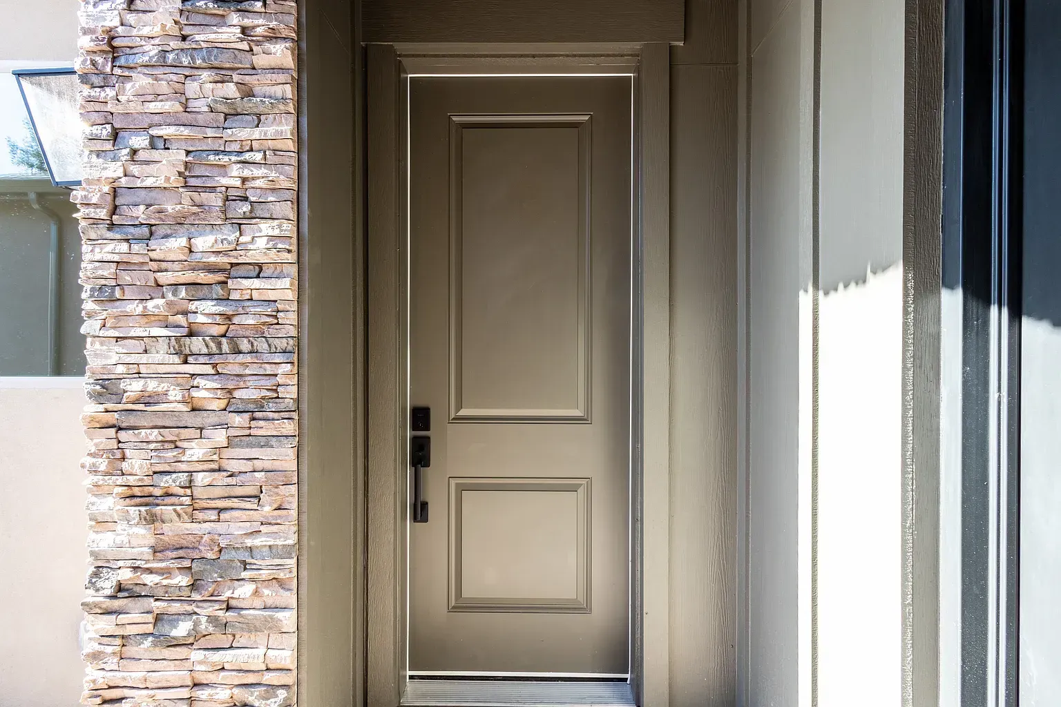Beige front door with black handle, surrounded by stone and light walls.