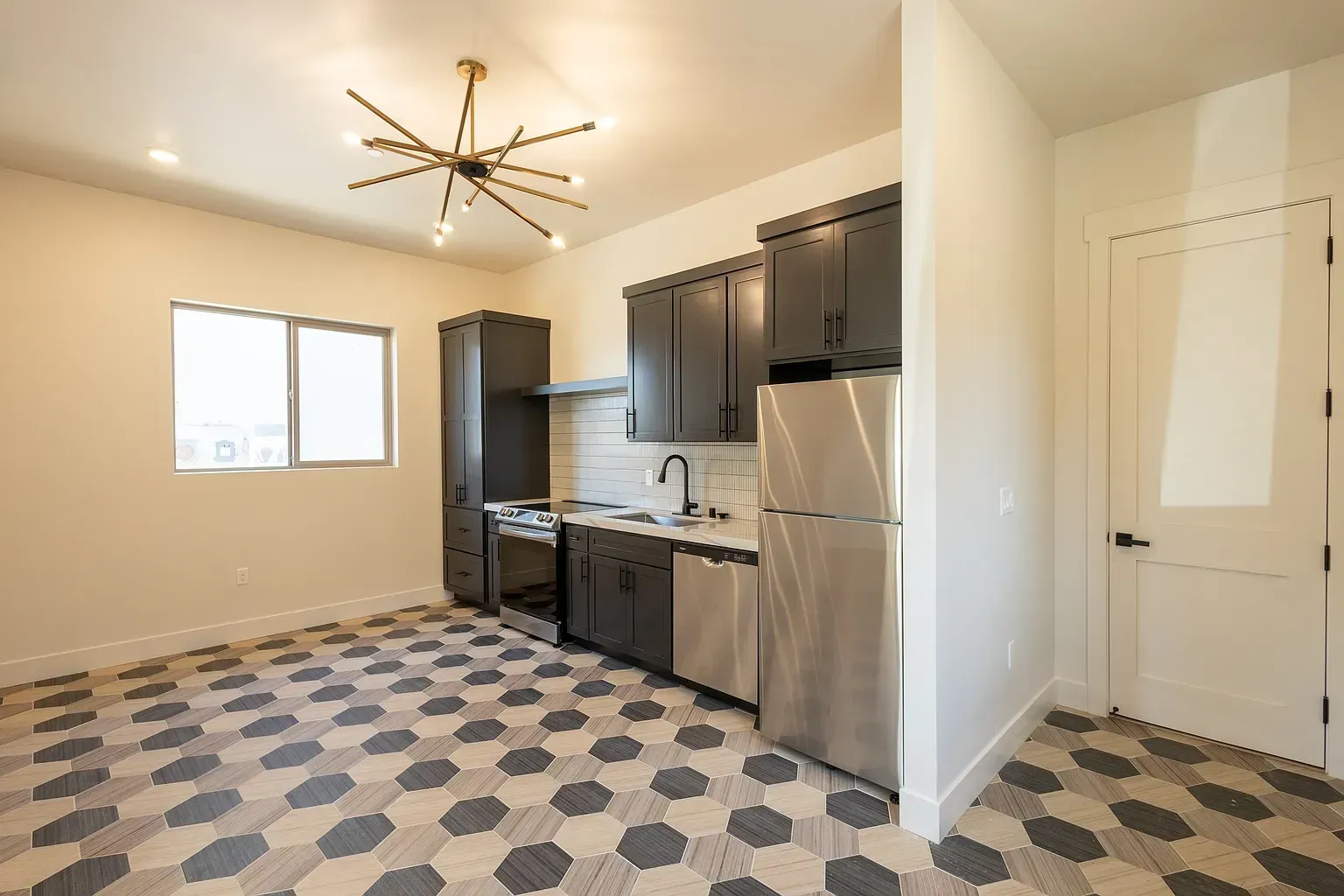 Kitchen with dark cabinets, stainless steel appliances, geometric patterned floor, and a starburst light fixture.