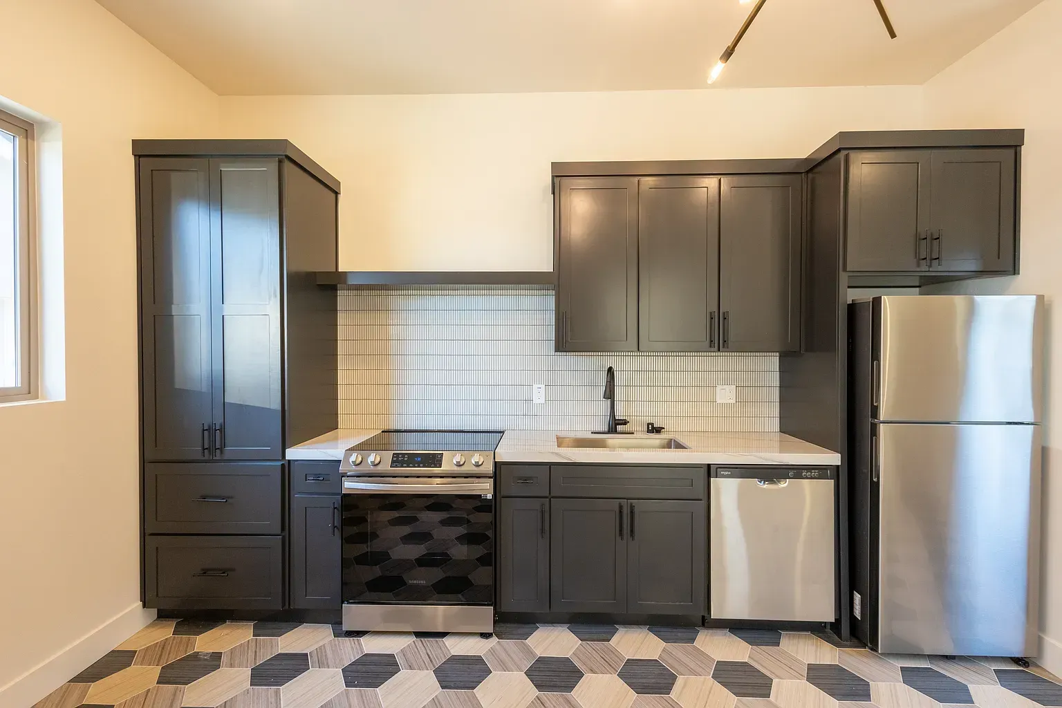 Small kitchen with dark gray cabinets, stainless steel appliances, and patterned floor.