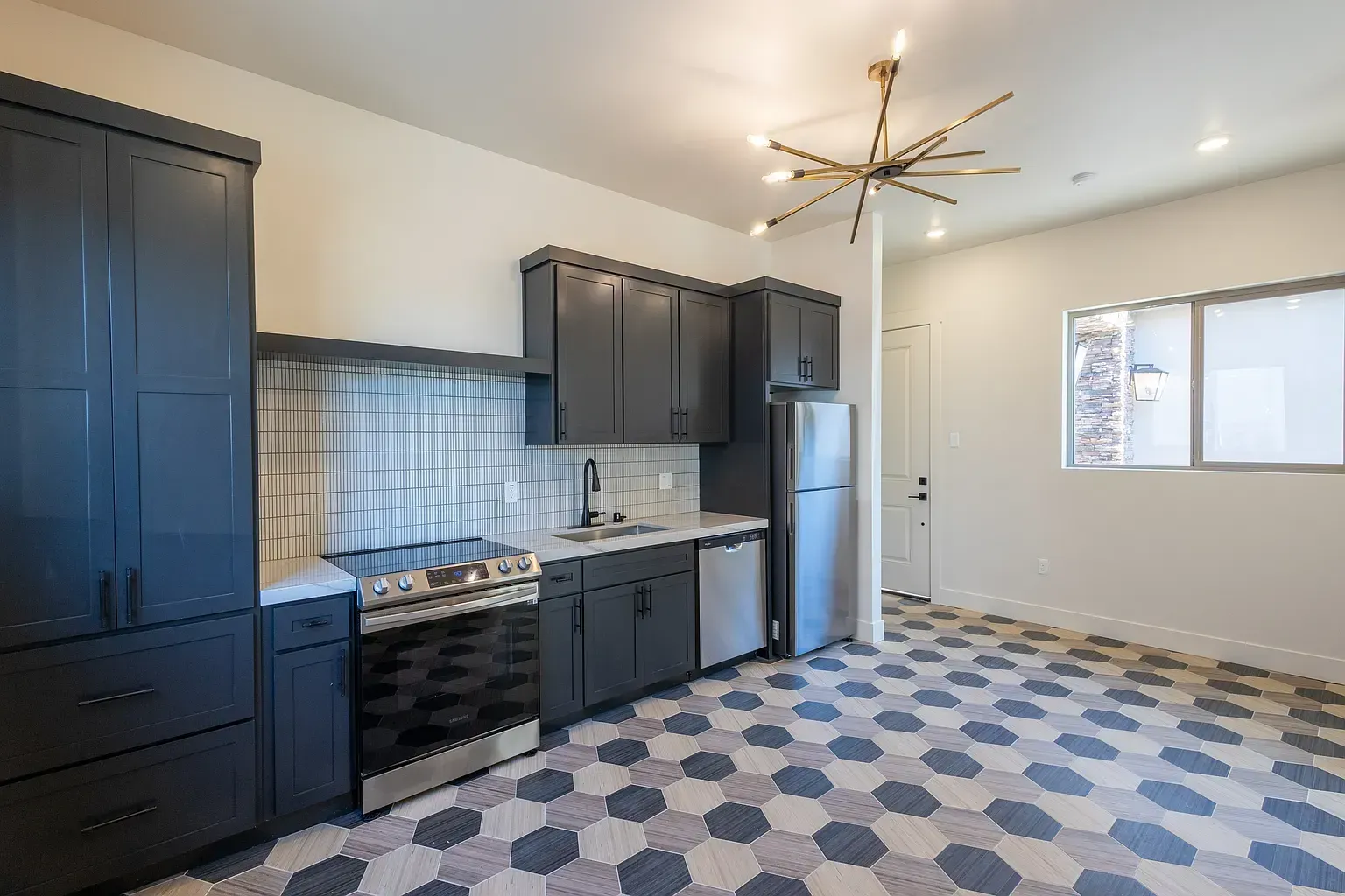 Modern kitchen with gray cabinets, stainless steel appliances, and patterned tile flooring.