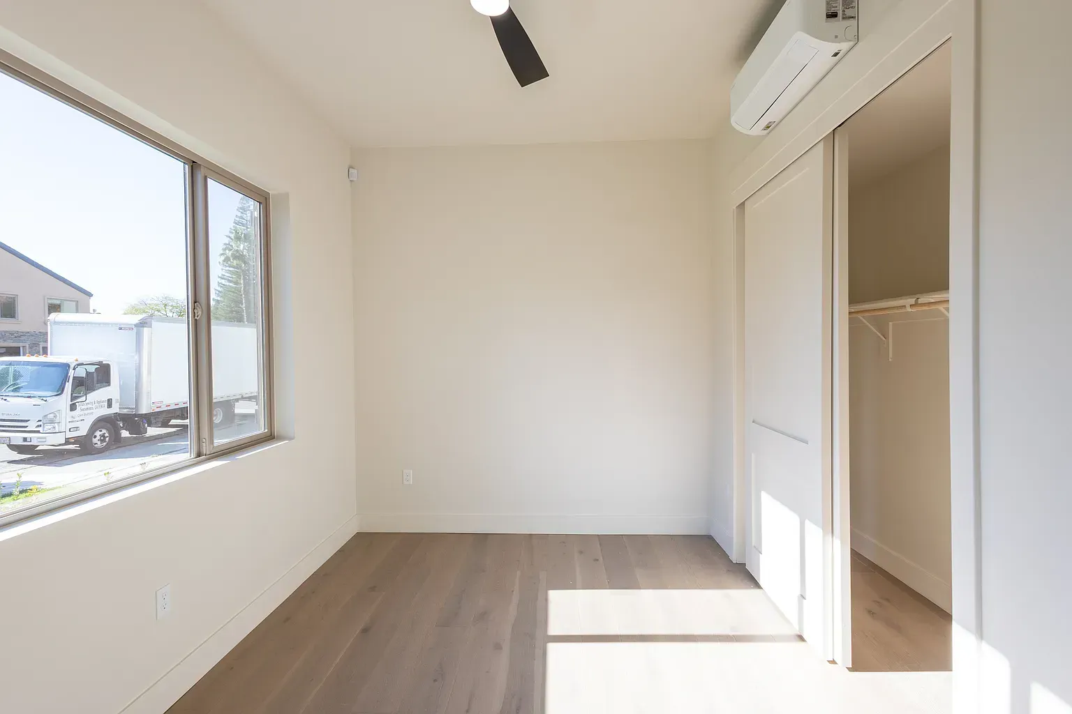 Empty room with a window, closet, and air conditioner. Bright, neutral colors, wood floor.