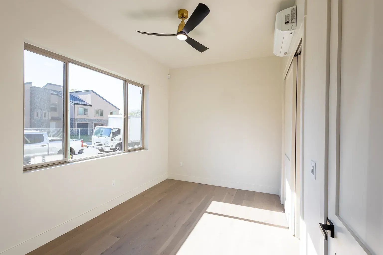 Empty room with a large window, hardwood floors, ceiling fan, and AC unit.