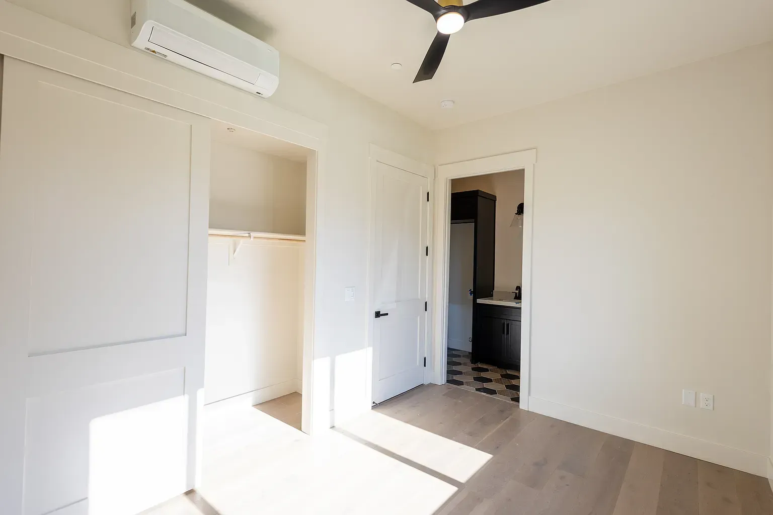 Empty bedroom with closet, door to bathroom, light wood floors, and air conditioner.
