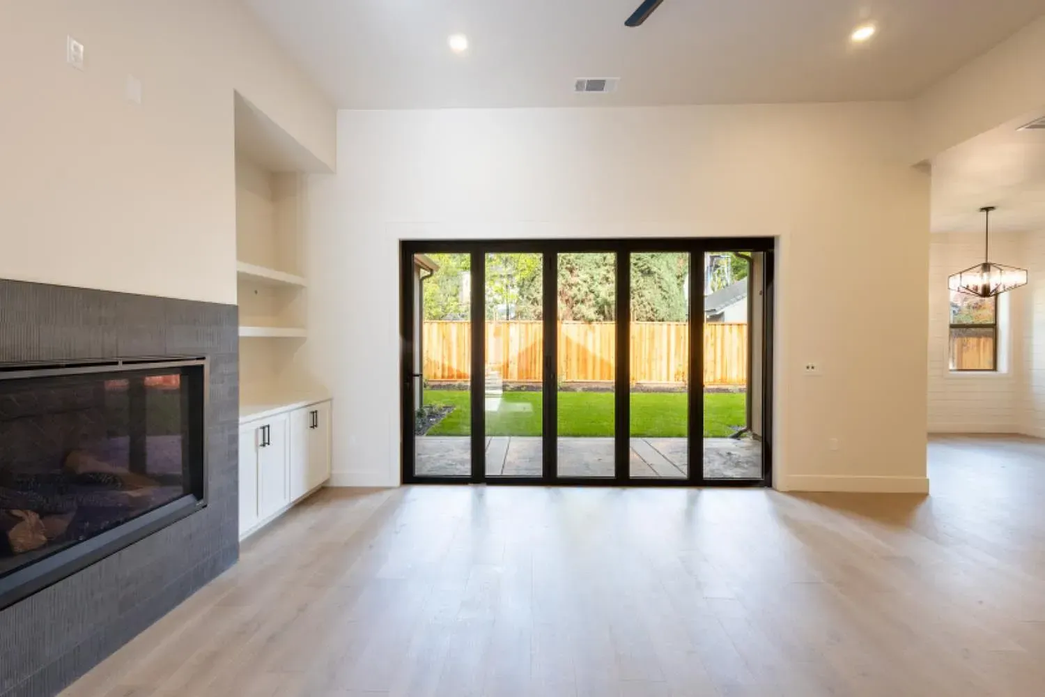 Modern living room with fireplace, built-in shelves, and folding glass doors opening to a backyard.