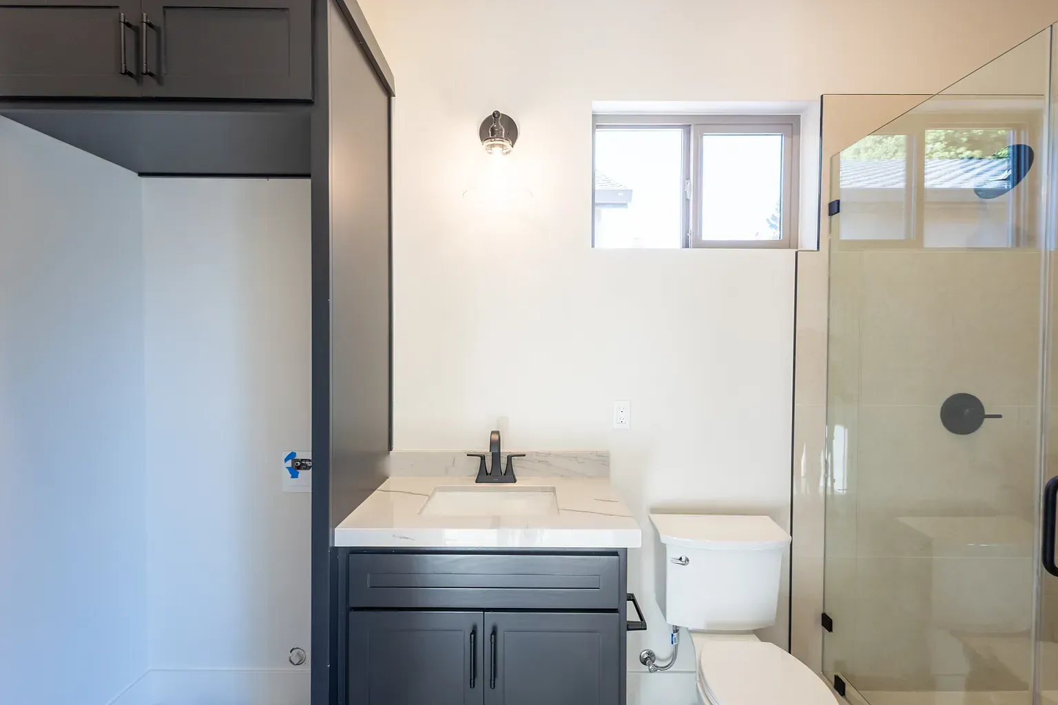 Bathroom interior with dark gray vanity, white toilet, and glass shower.