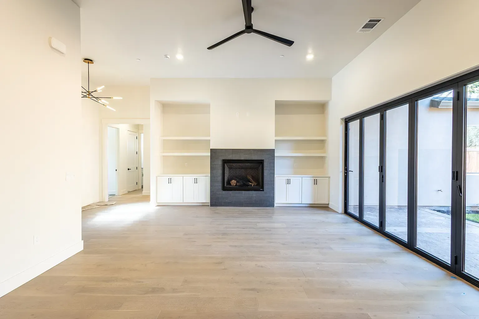 Empty, modern living room with fireplace, built-ins, and large glass doors.