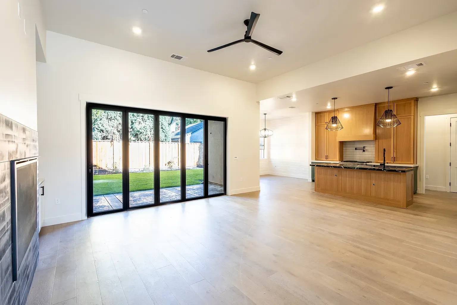 Spacious, modern living area with folding glass doors, wooden floors, and kitchen with island.