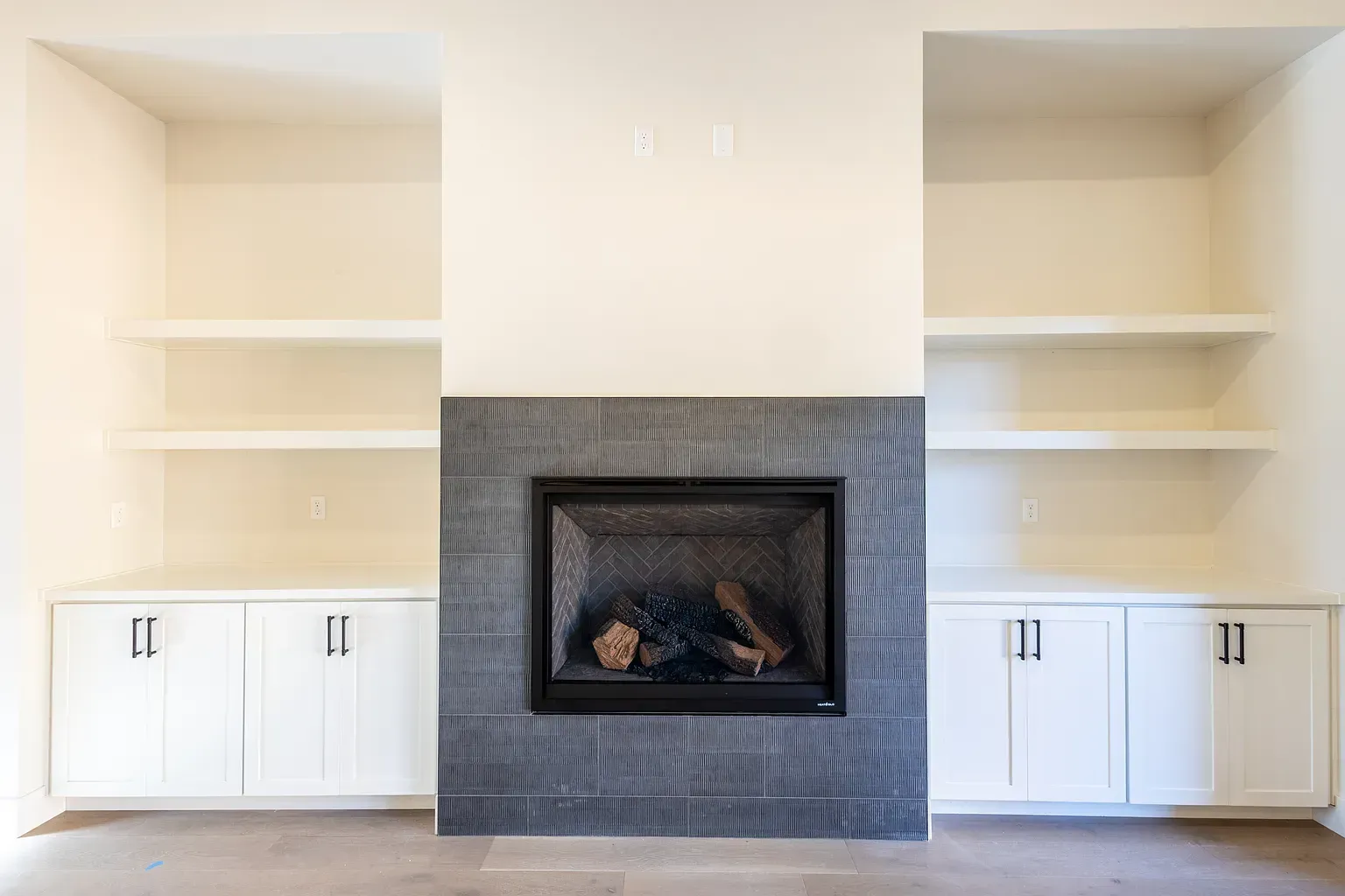 Fireplace with gray tile surround, flanked by white built-in shelving and cabinets.