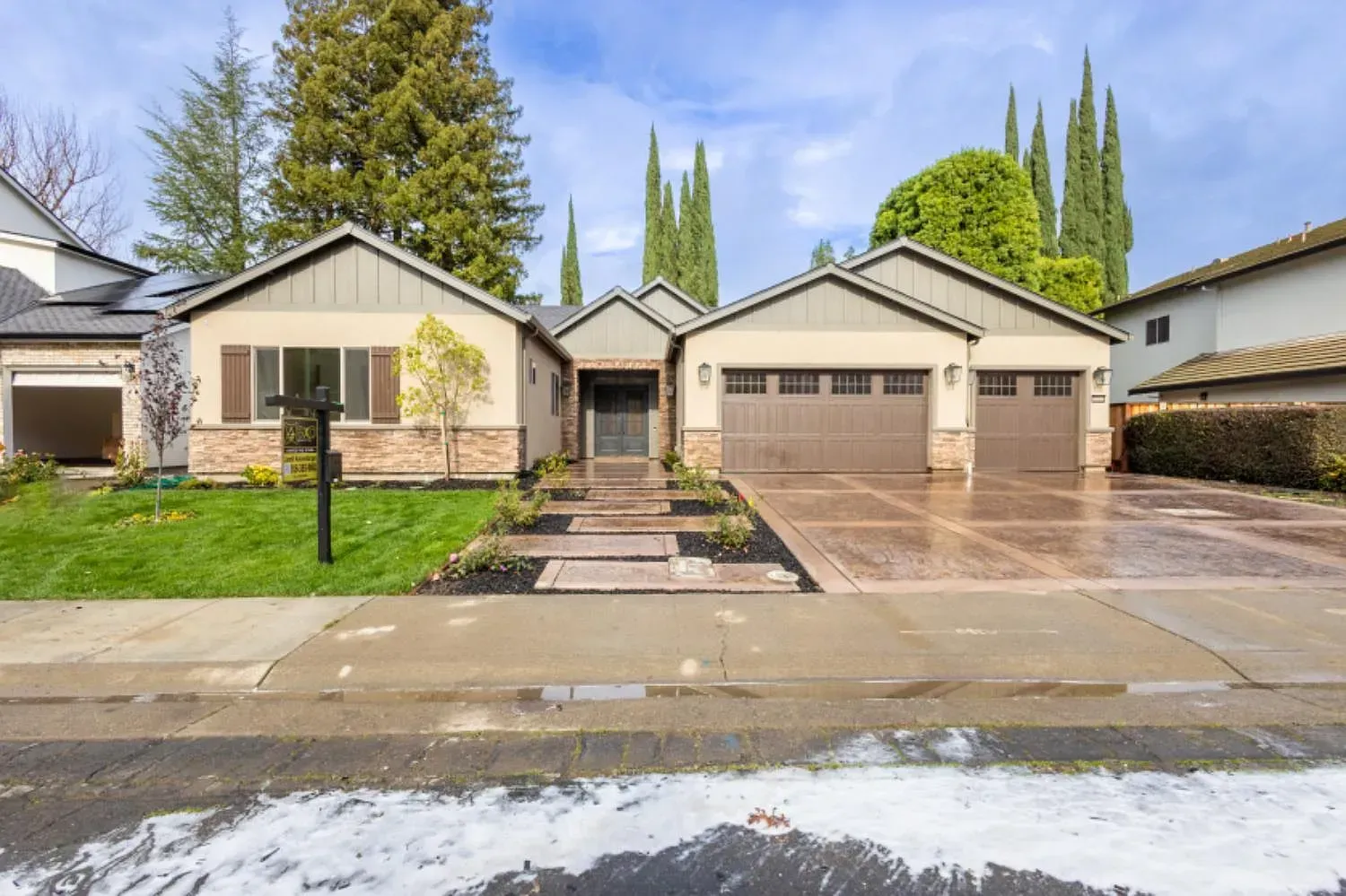 Tan and brown single-story house with a two-car garage, front walkway, and green landscaping.