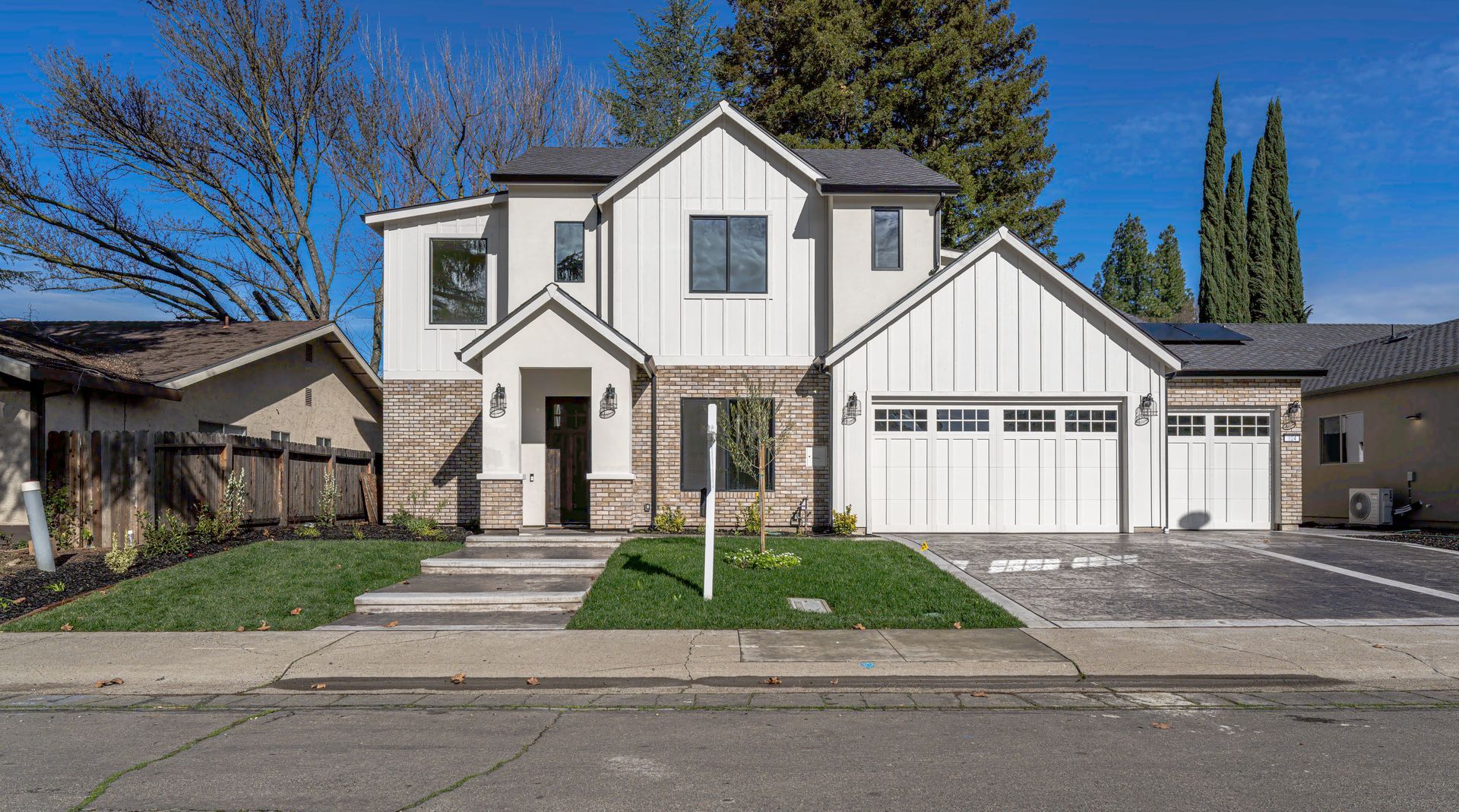 Modern two-story house with white siding and gray roof, two-car garage, and small front yard with green lawn.