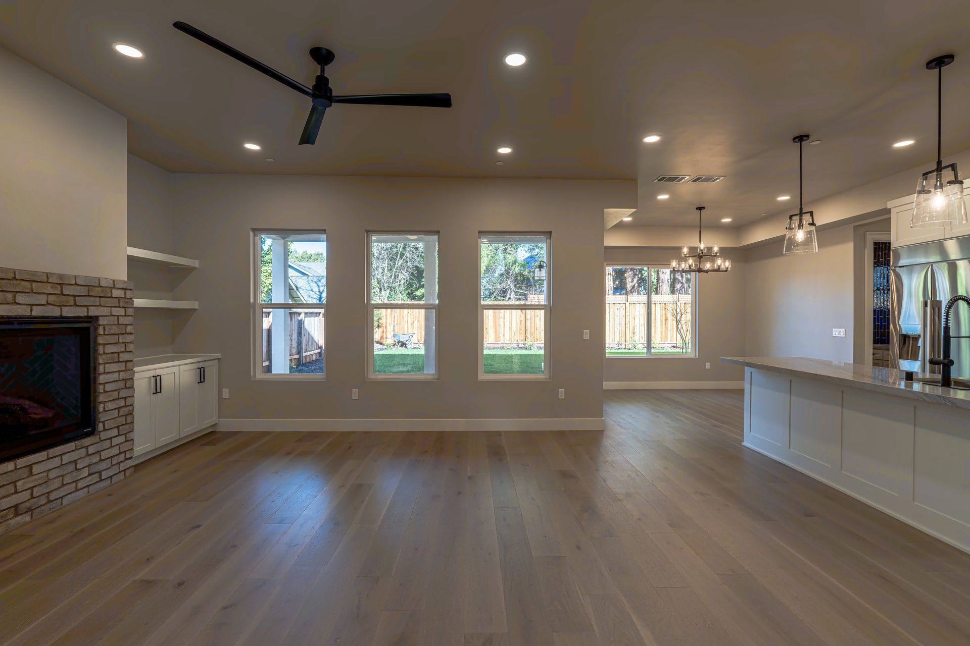 Spacious, modern living room with fireplace, three windows, and wooden floors.