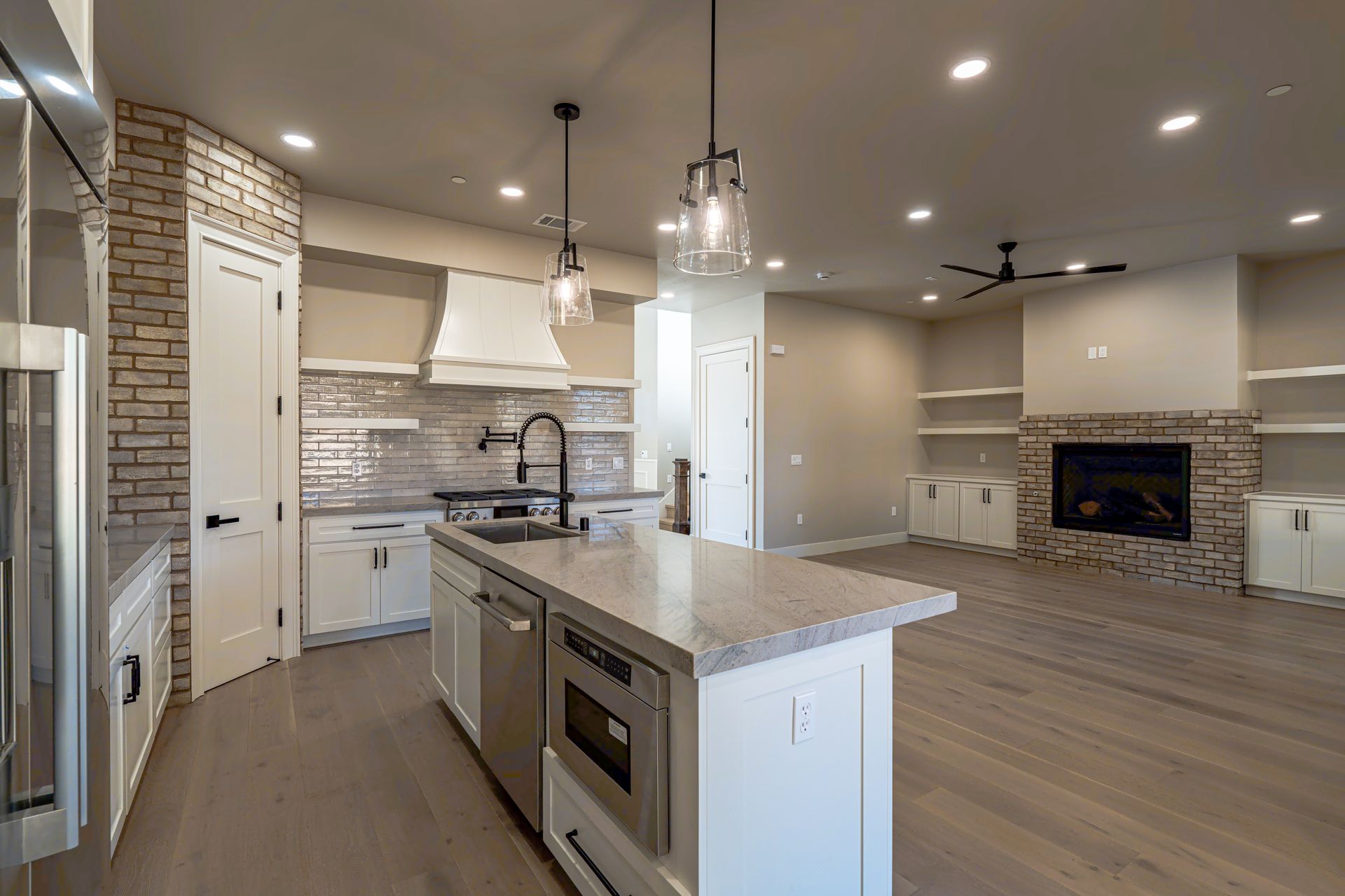 Modern kitchen with island, white cabinets, brick accents, and fireplace in an open-concept living space.