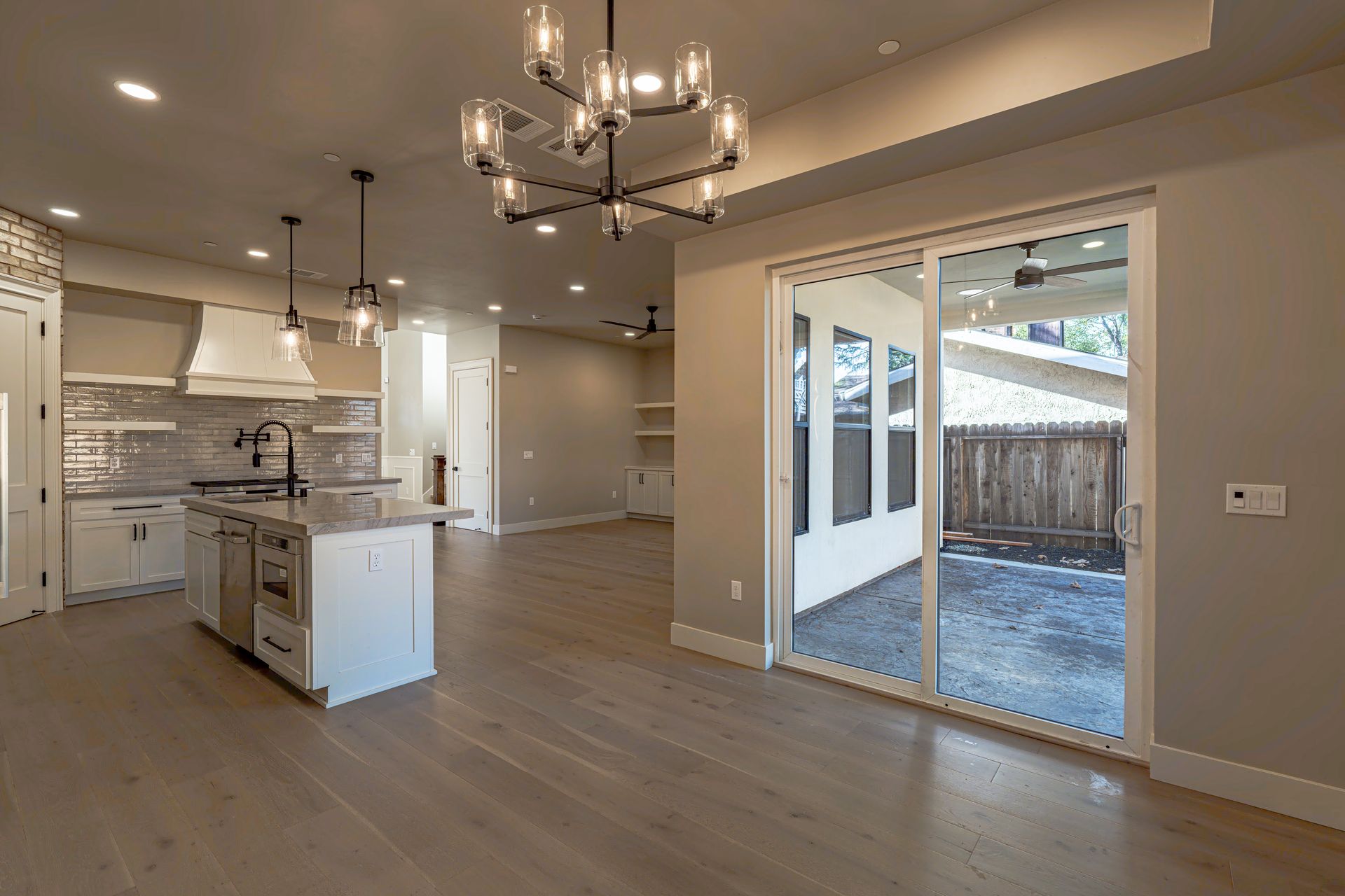 Open kitchen with island, modern lighting, and sliding glass door to patio with wood fence.