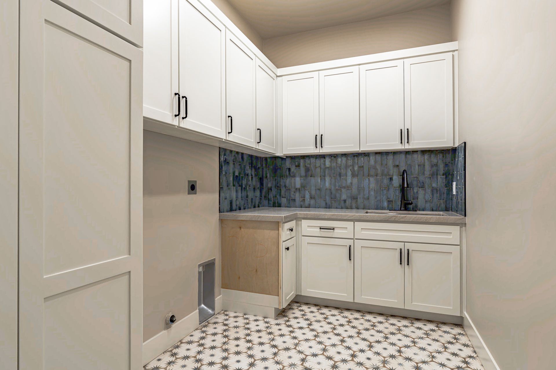 White laundry room with cabinets, dark backsplash, patterned floor.