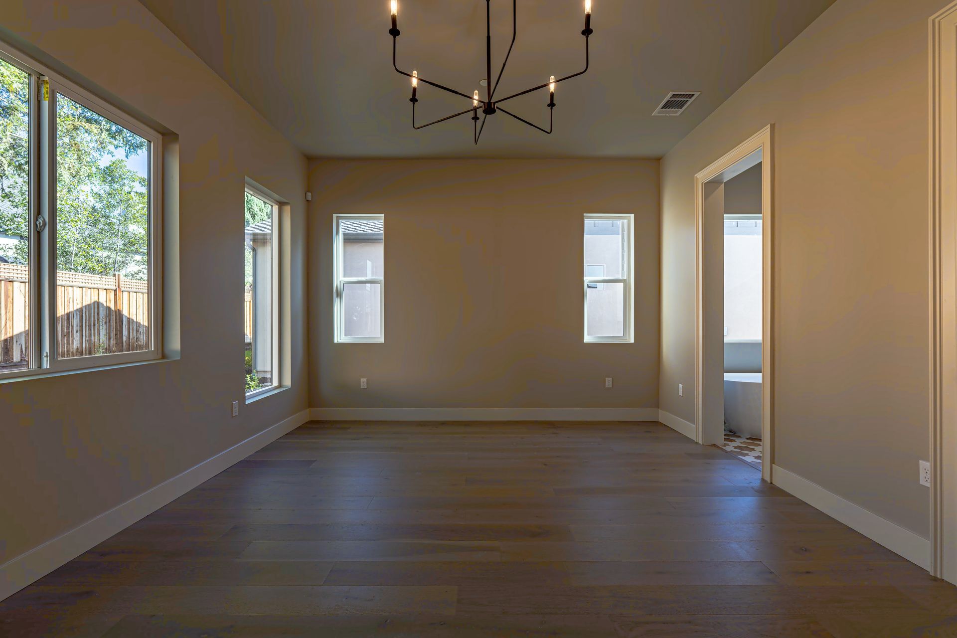 Empty dining room with wooden floor, tan walls, windows, and chandelier.