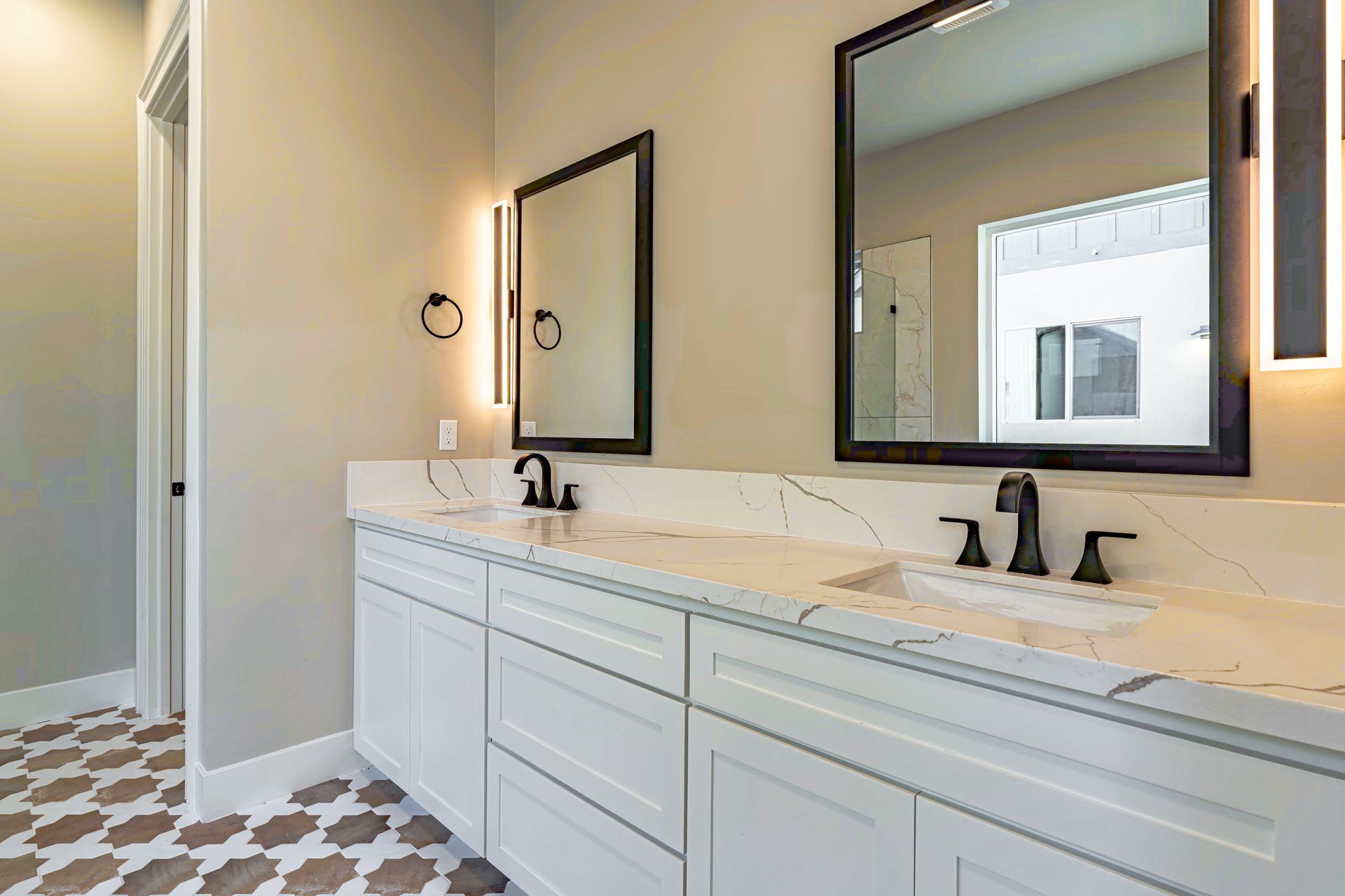 Bathroom with white vanity, black framed mirrors, and patterned floor.