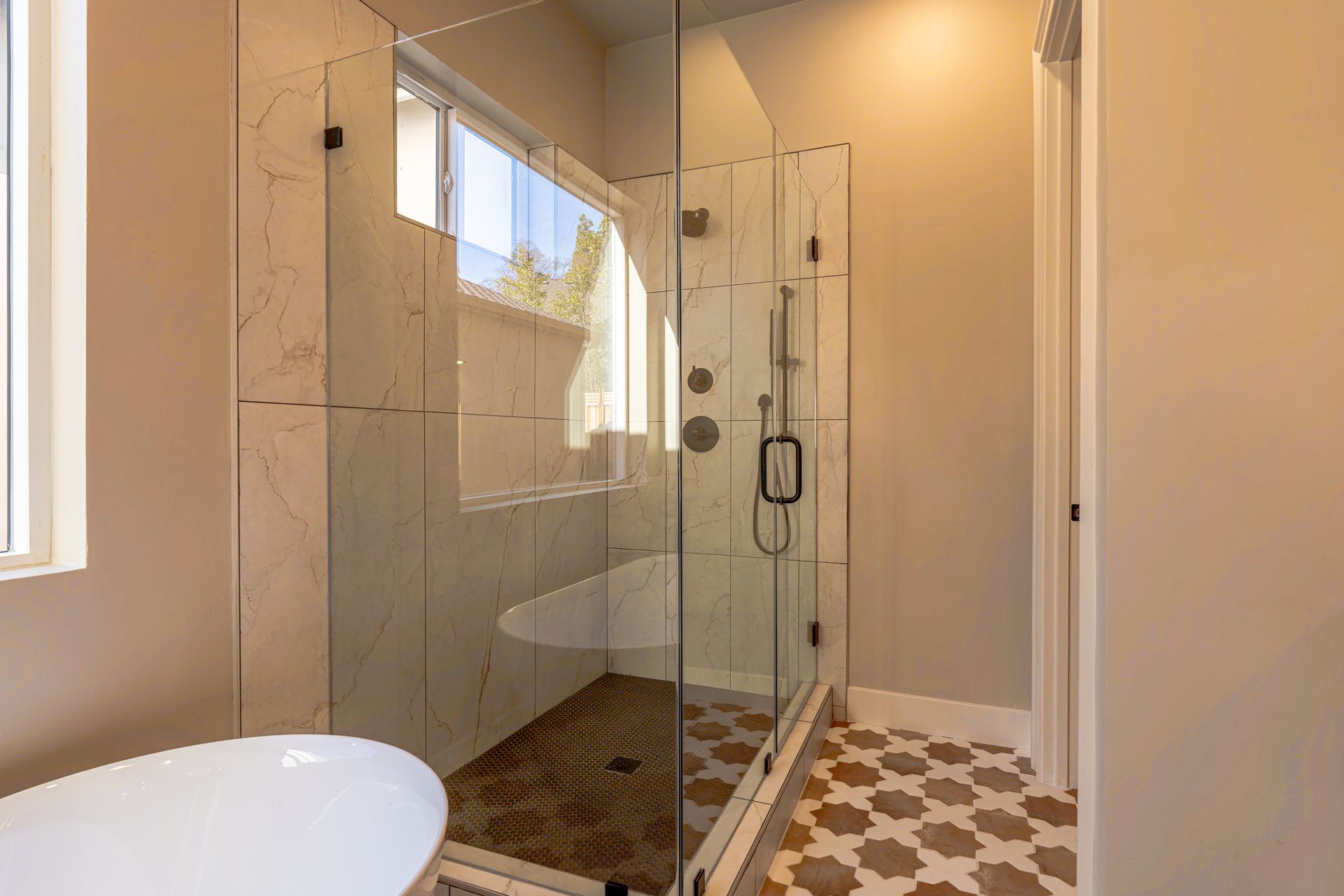 Bathroom with a glass shower, marble tile, and patterned floor.