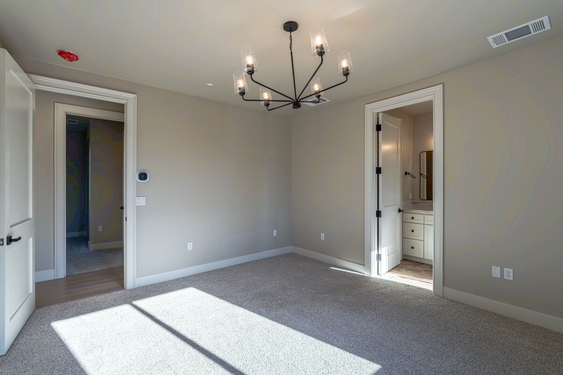 Empty bedroom with neutral walls, gray carpet, and a chandelier. Two doorways lead to other rooms.