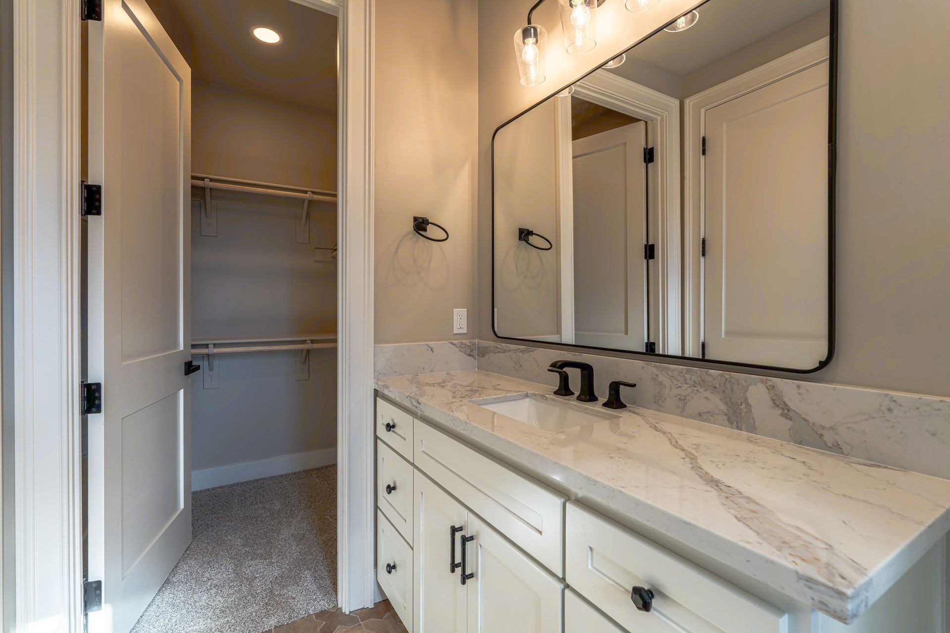 Bathroom with white cabinets, marble countertop, large mirror, and open closet.