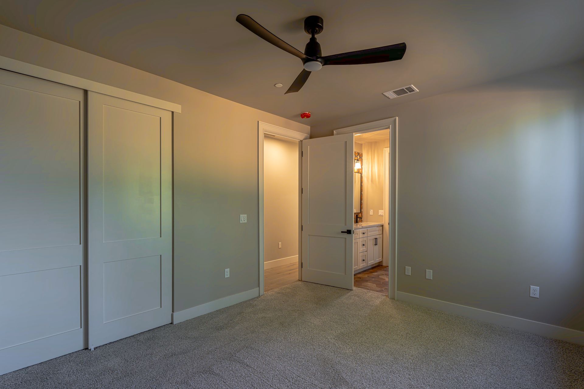 Bedroom with closet and doorway to bathroom, gray walls, beige carpet, ceiling fan.