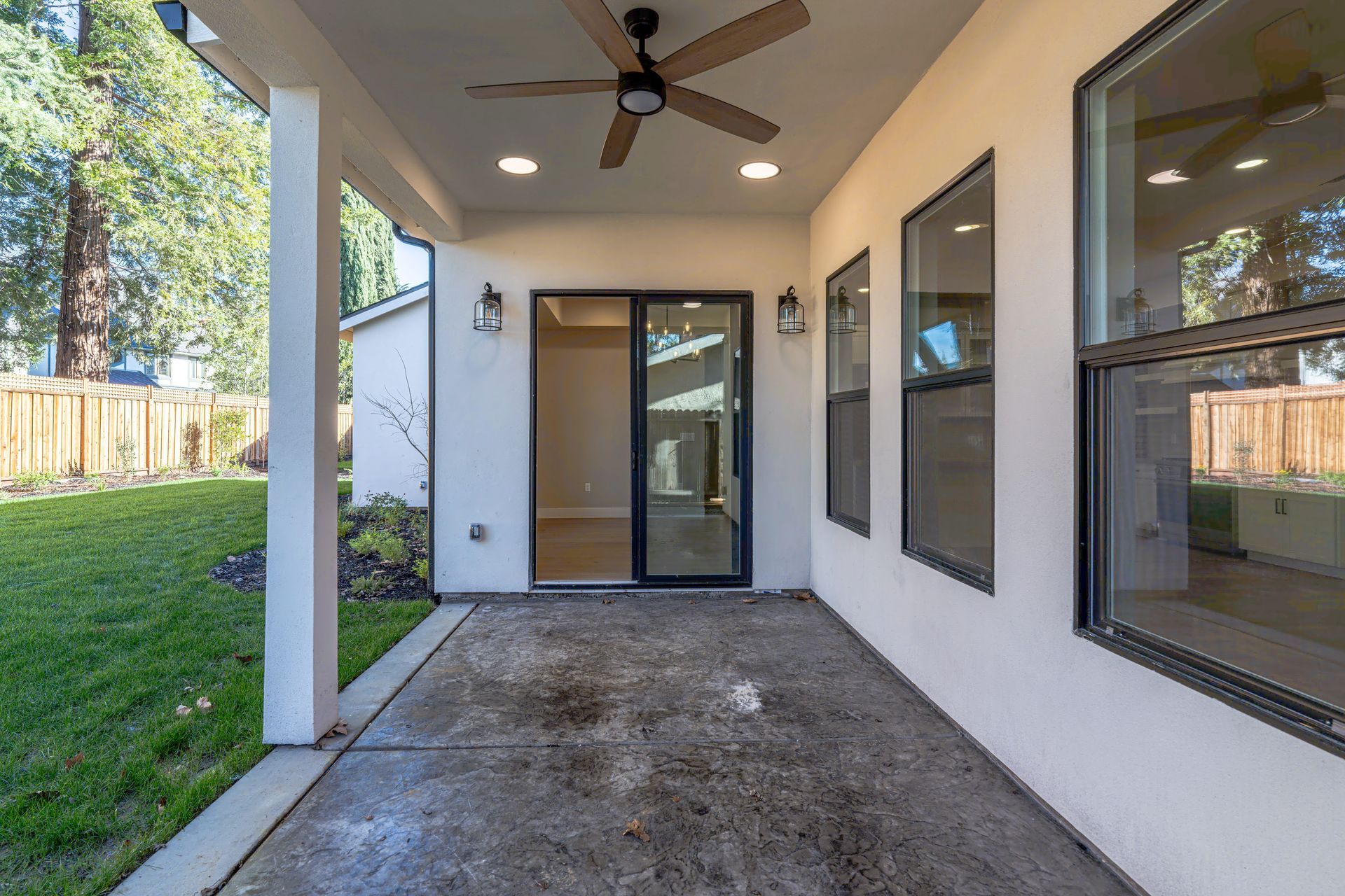 Covered patio with sliding glass door and windows, overlooking a grassy backyard.