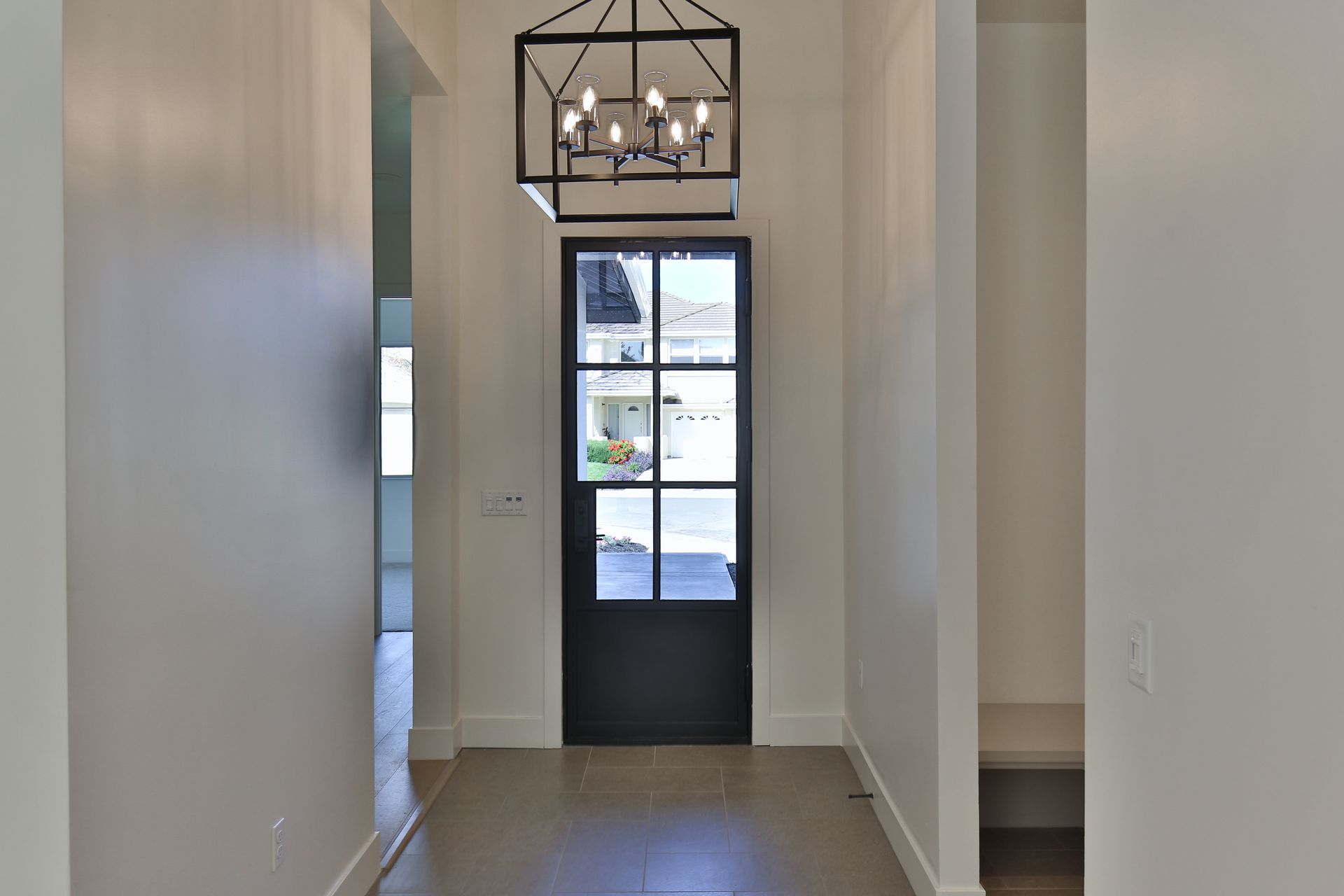 A hallway with a black door and a chandelier hanging from the ceiling.