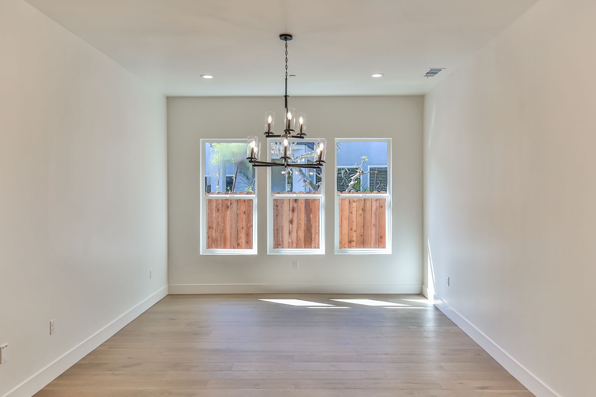 An empty room with a chandelier hanging from the ceiling and three windows.