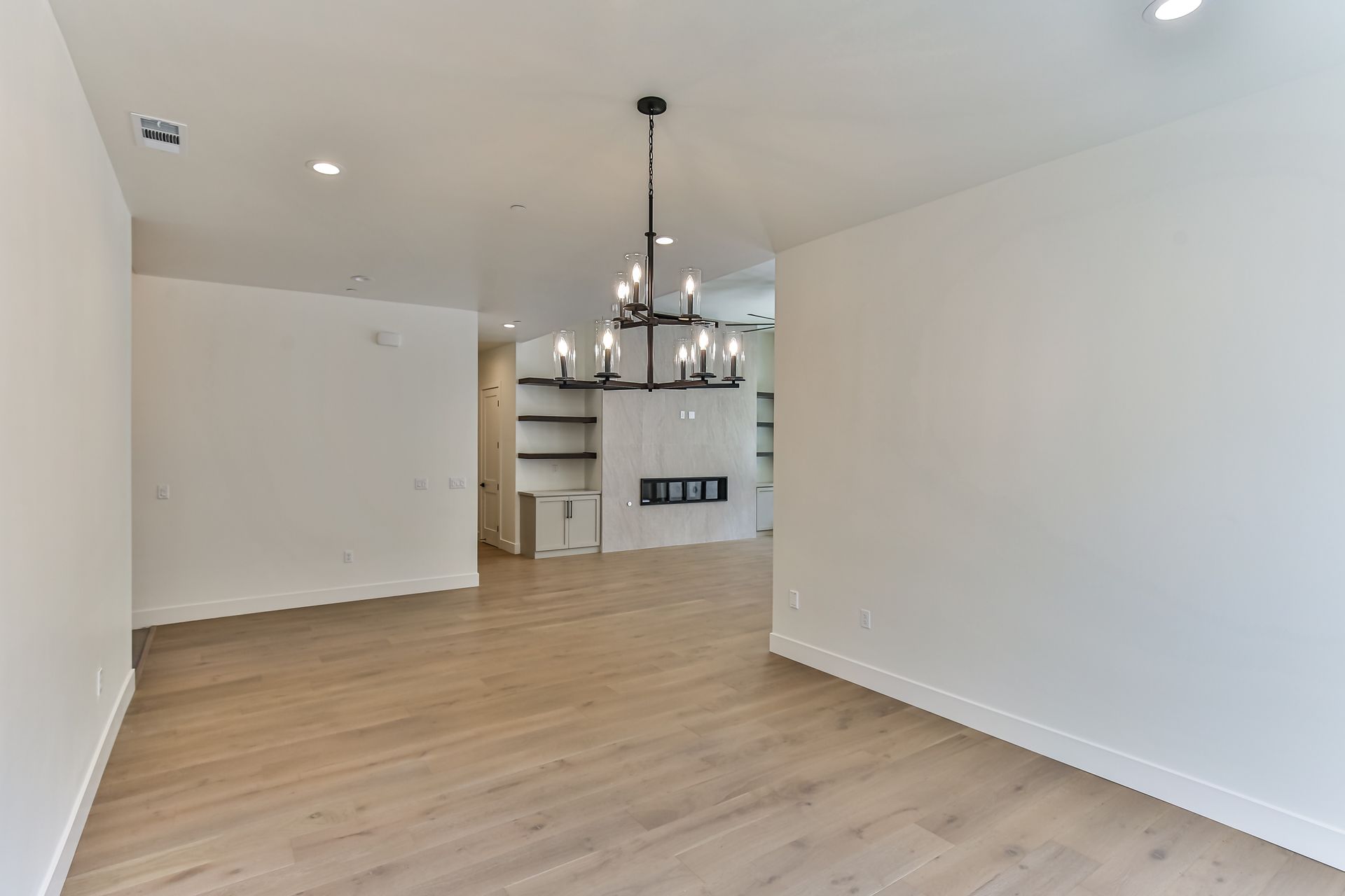 An empty living room with hardwood floors and a chandelier hanging from the ceiling.