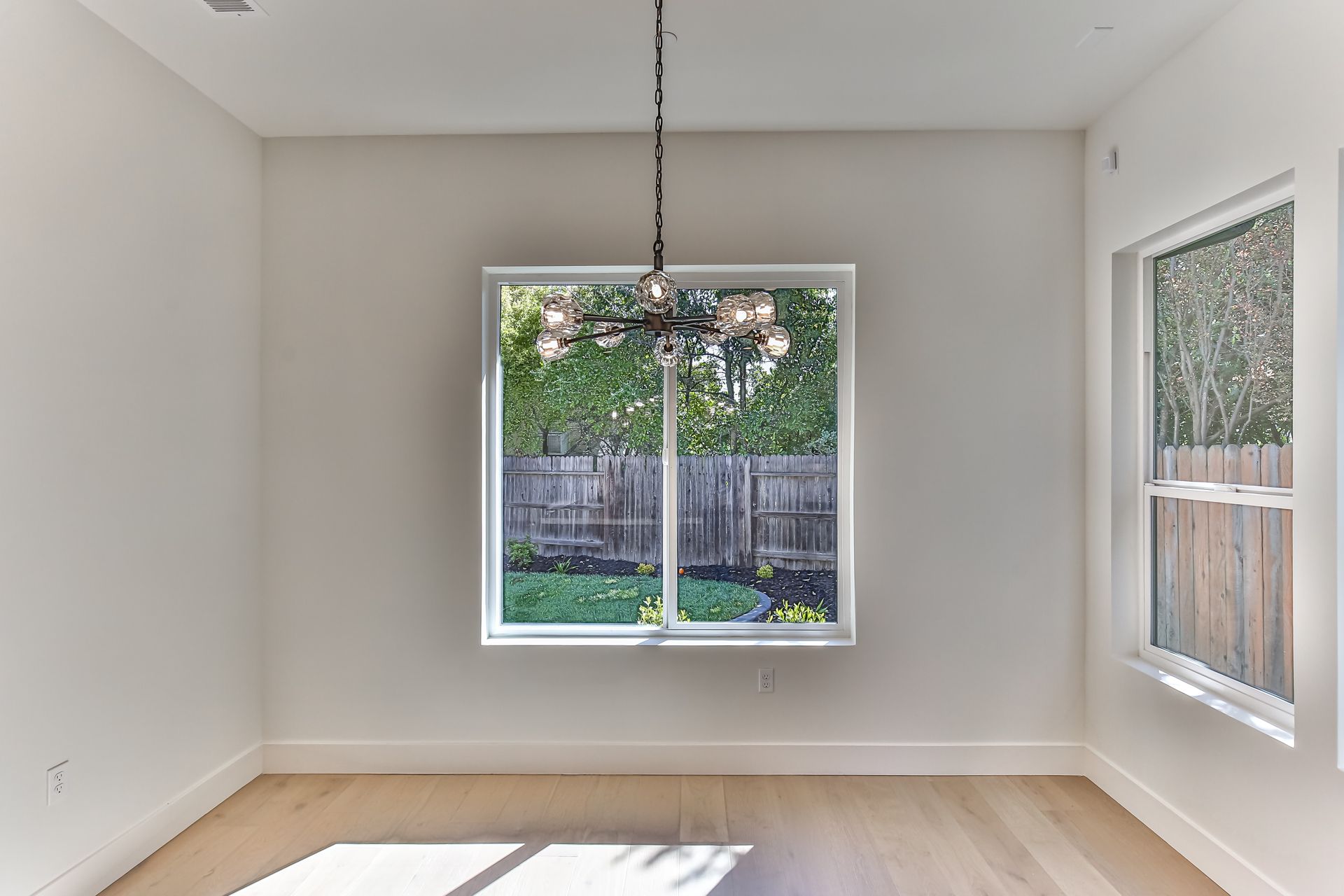 An empty room with two windows and a chandelier hanging from the ceiling.