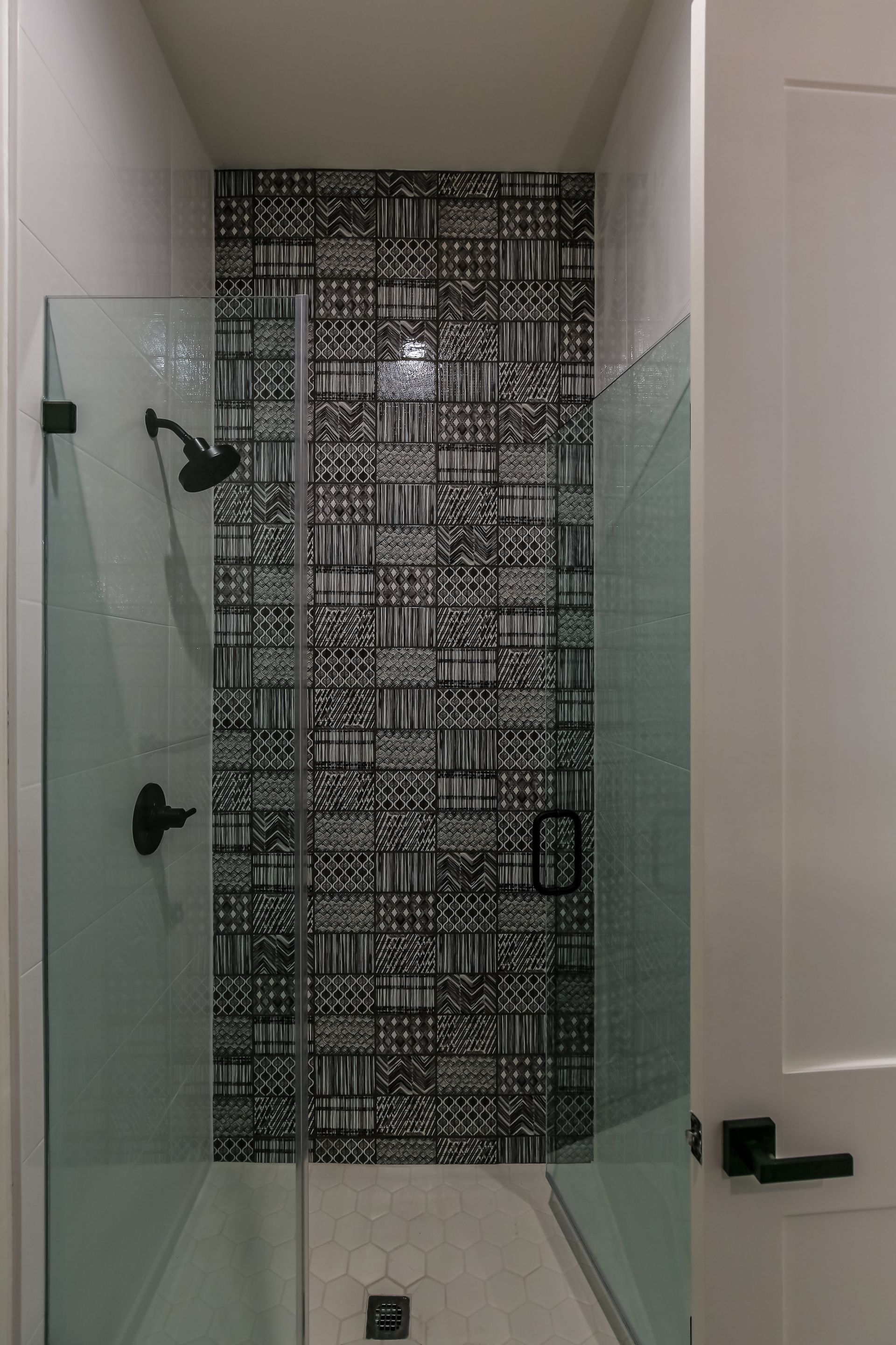 A walk in shower with a black and white tile wall and a glass door.