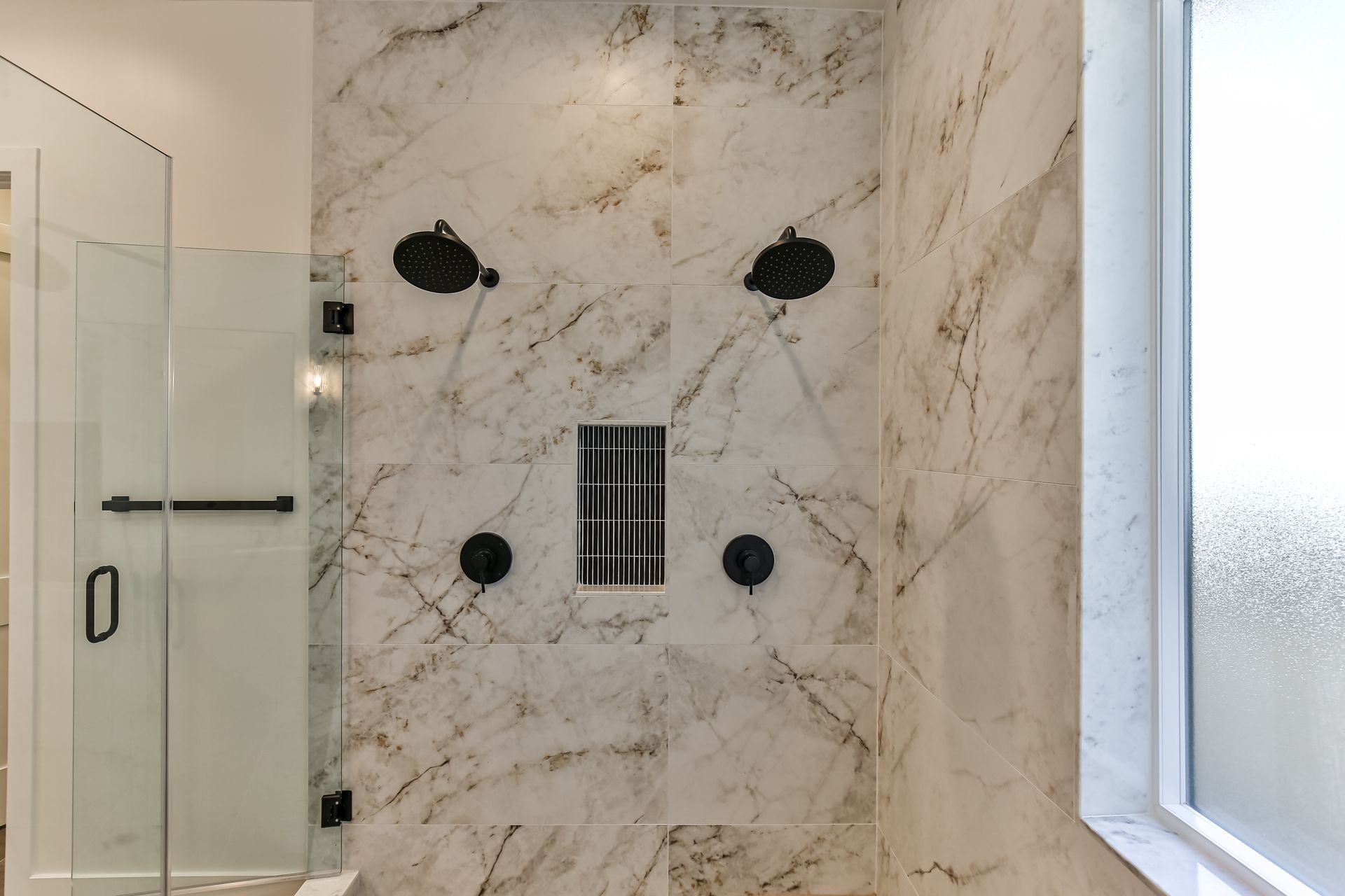 A bathroom with marble walls , a walk in shower , and a window.